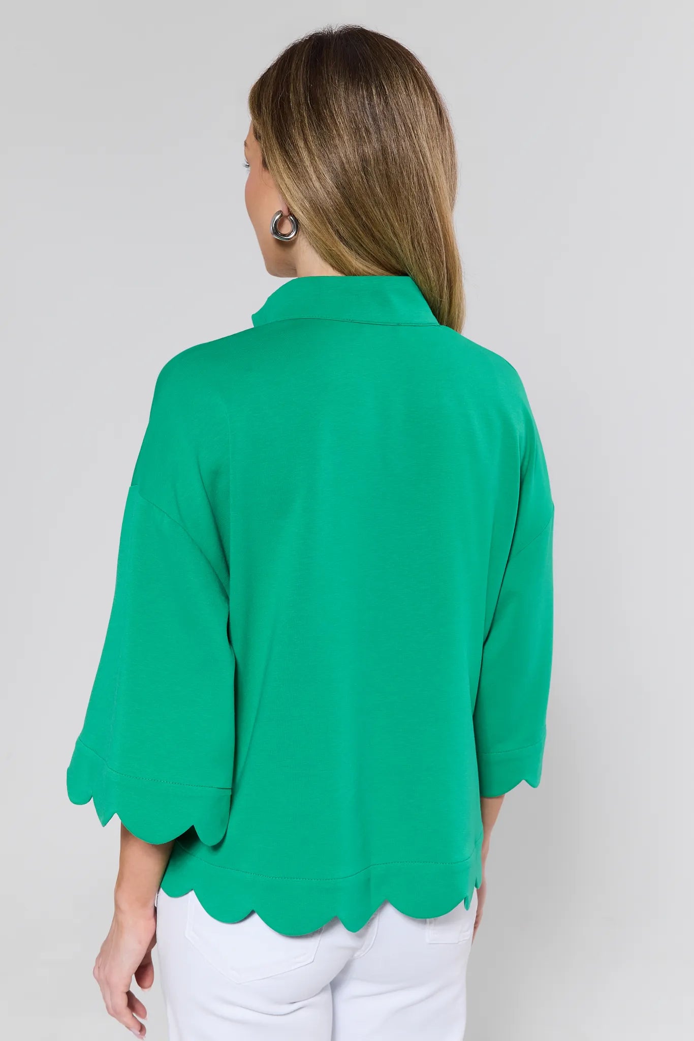 Green blouse with scalloped hem worn by a person on a plain background