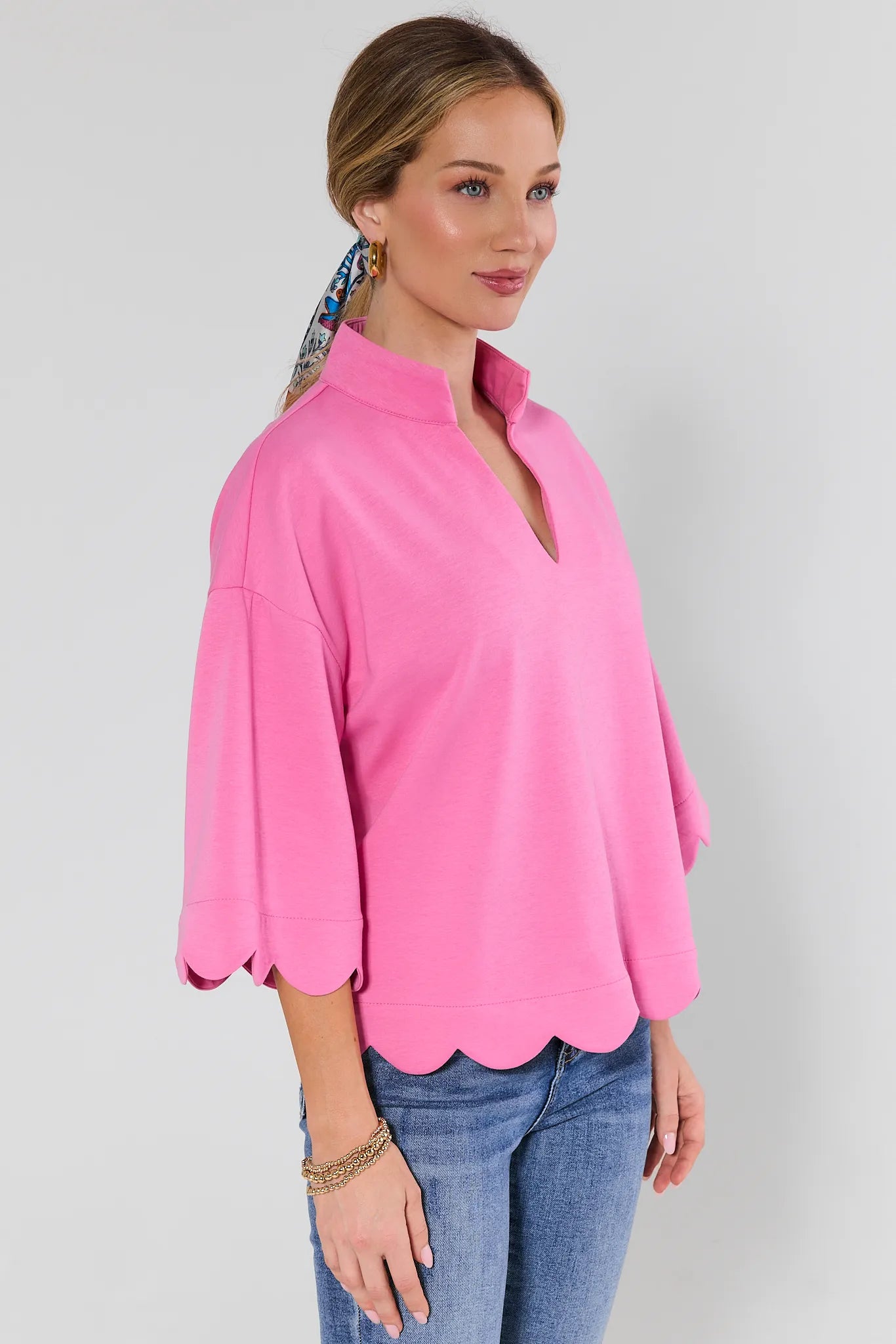 Woman wearing a pink blouse with scalloped hem and blue jeans on a plain background