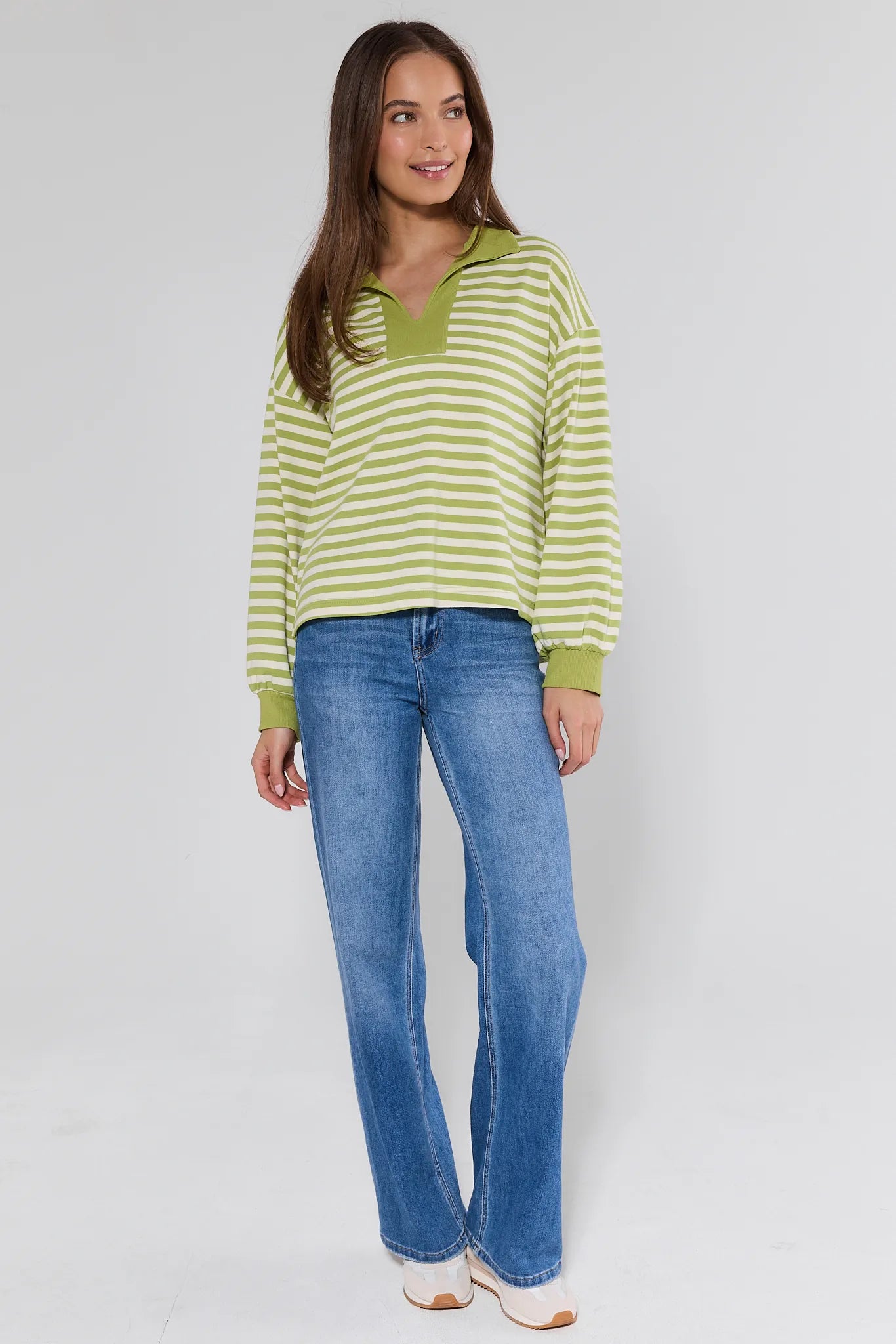 woman wearing green sweater with stripes and jeans on white background