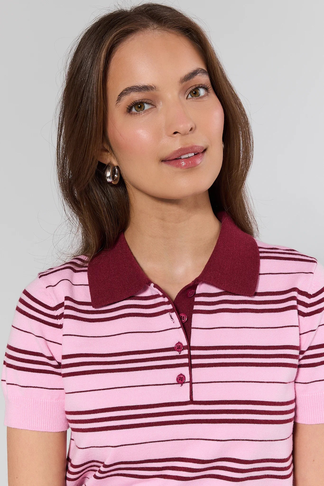 Woman wearing a pink and maroon striped polo shirt against a plain background