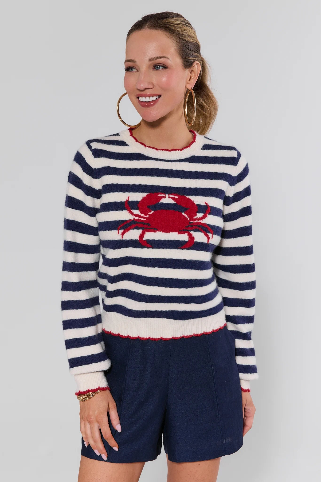 Woman wearing a navy and white striped sweater with a red crab design on a plain background
