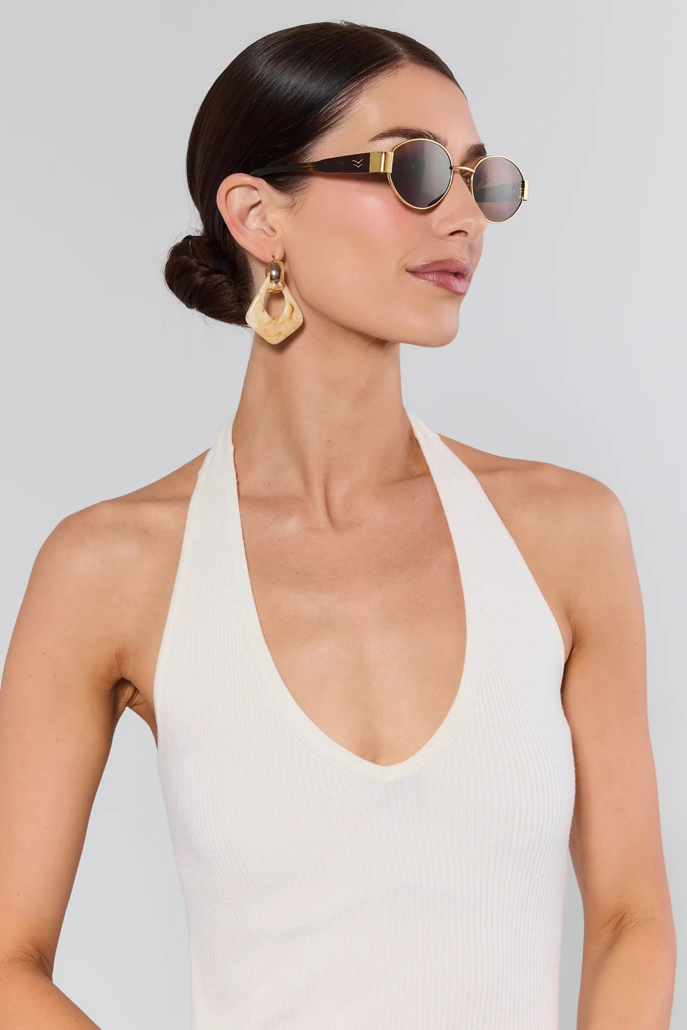 Woman wearing sunglasses and a white halter top against a plain background