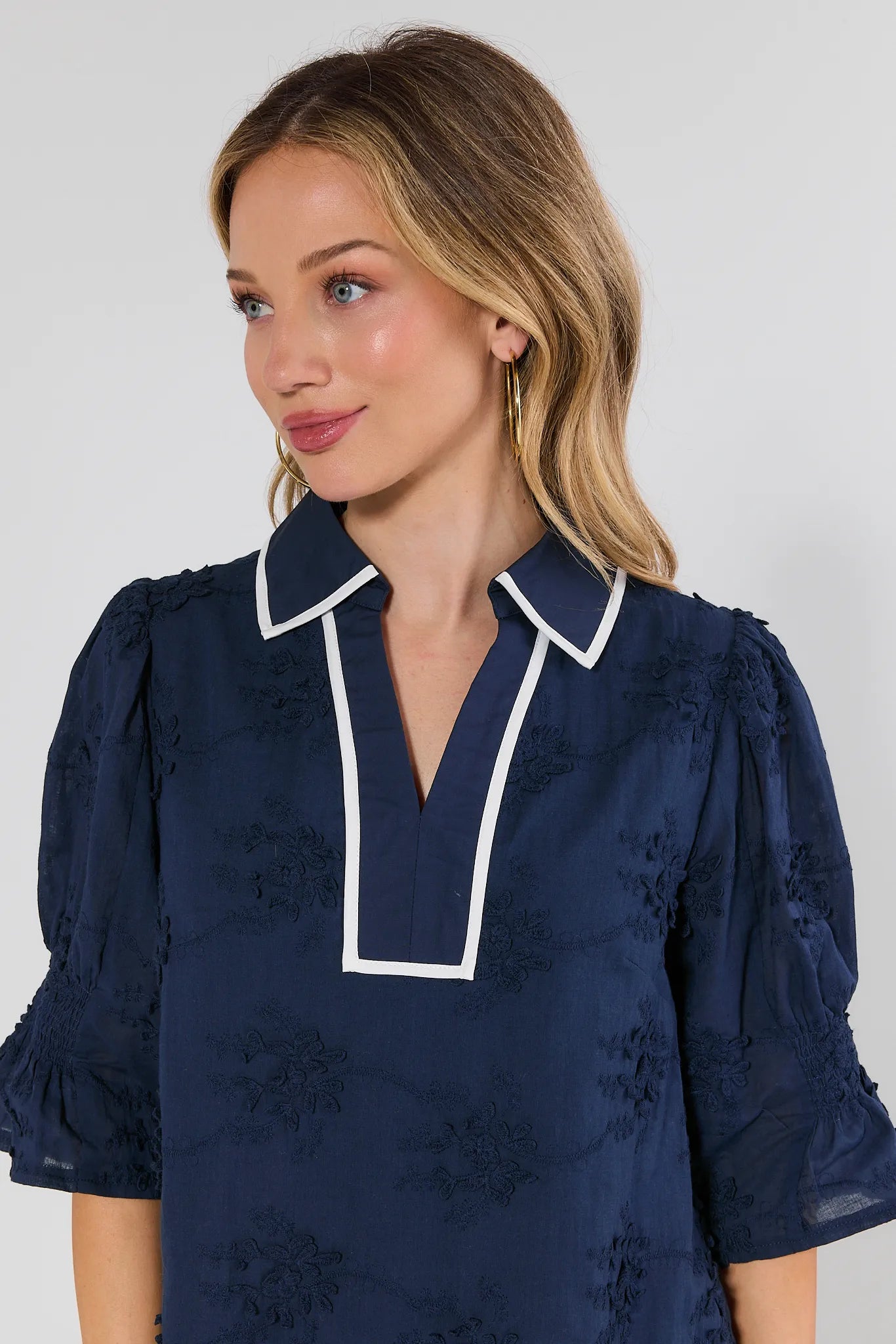Woman wearing a navy blue dress with white trim on a plain background