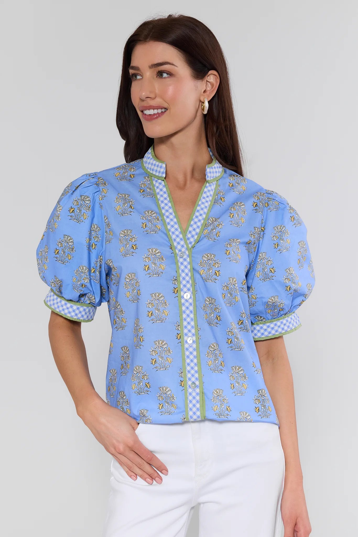 Woman wearing a blue patterned blouse with white pants on a plain background