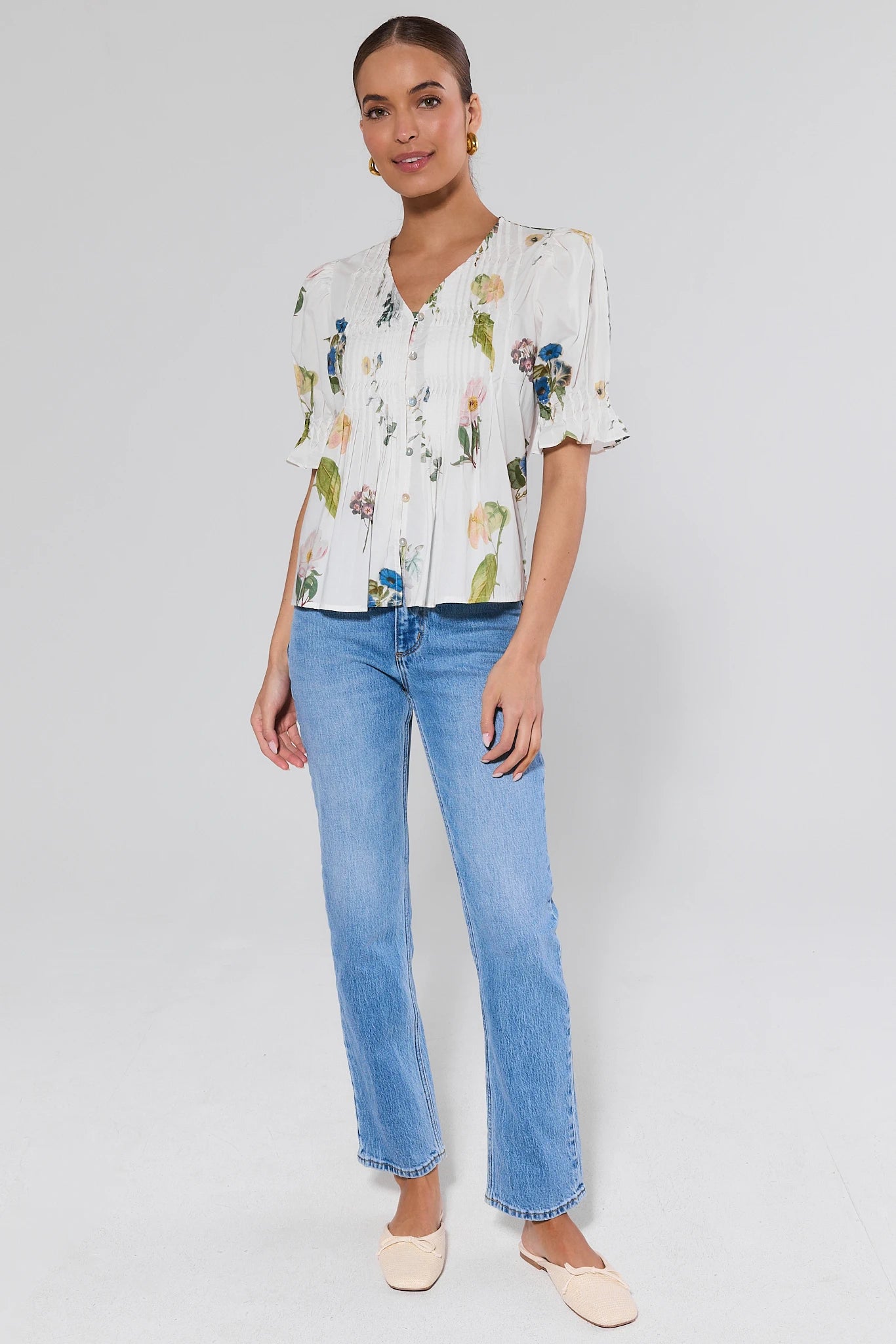 Woman wearing a floral blouse and blue jeans on a plain background