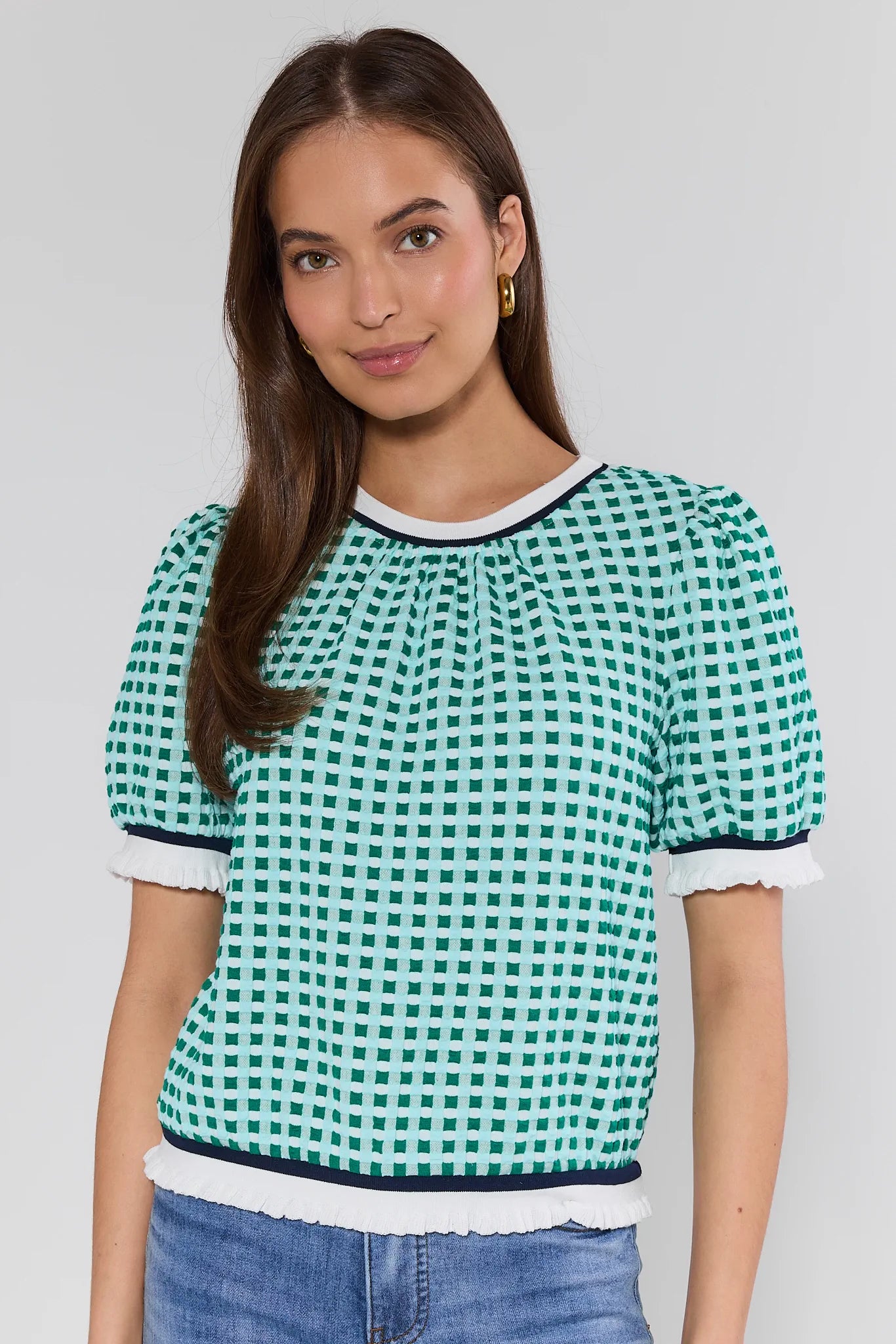 Woman wearing a green and white checkered blouse with blue jeans on a plain background