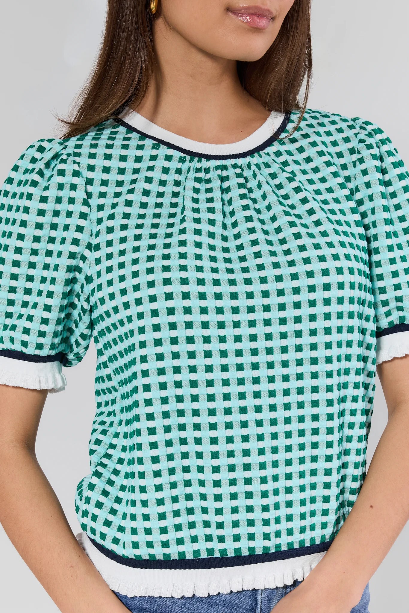 Green and white checkered top worn by a person on a plain background