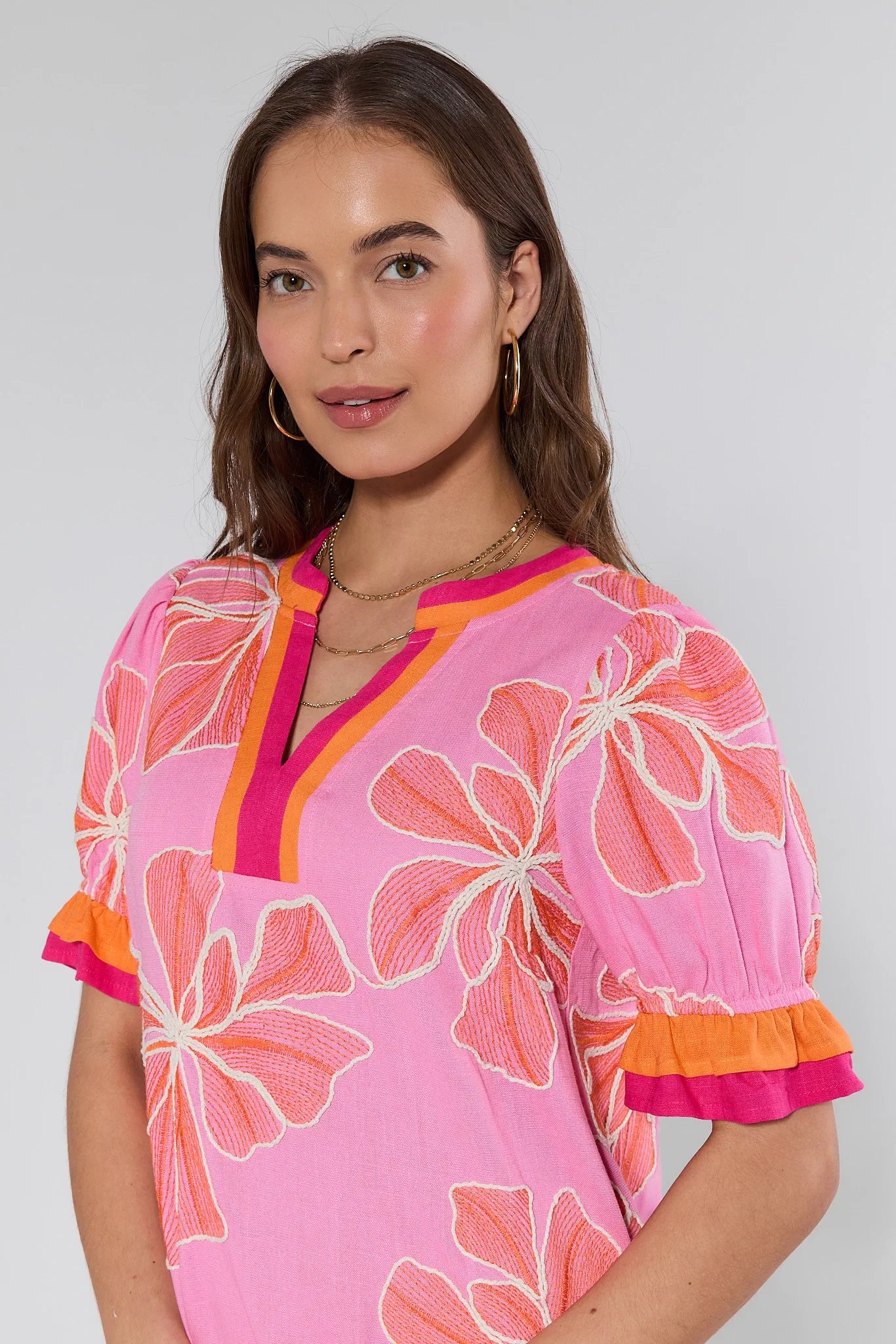 Woman wearing a pink floral dress with orange accents on a plain background
