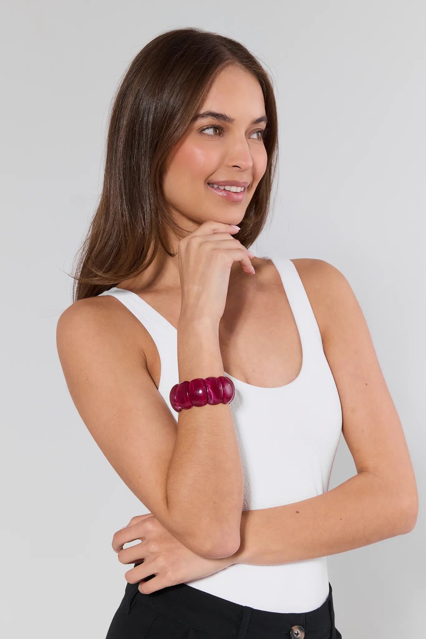 Woman wearing a white tank top and black pants with a red bracelet on a light gray background