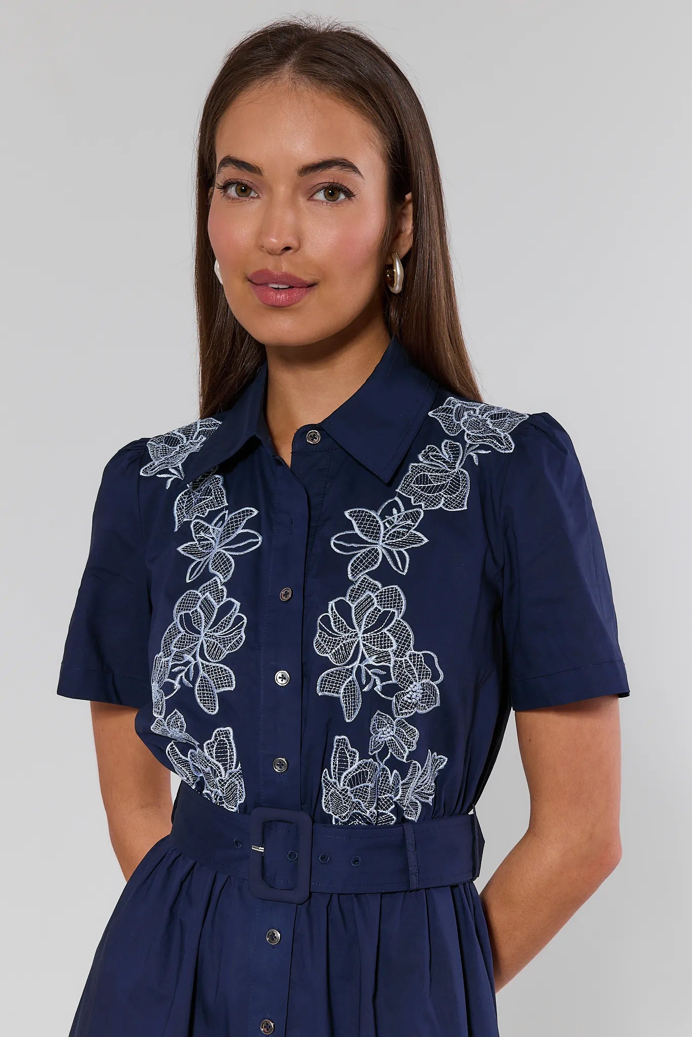 Woman wearing a navy dress with white floral embroidery on a plain background