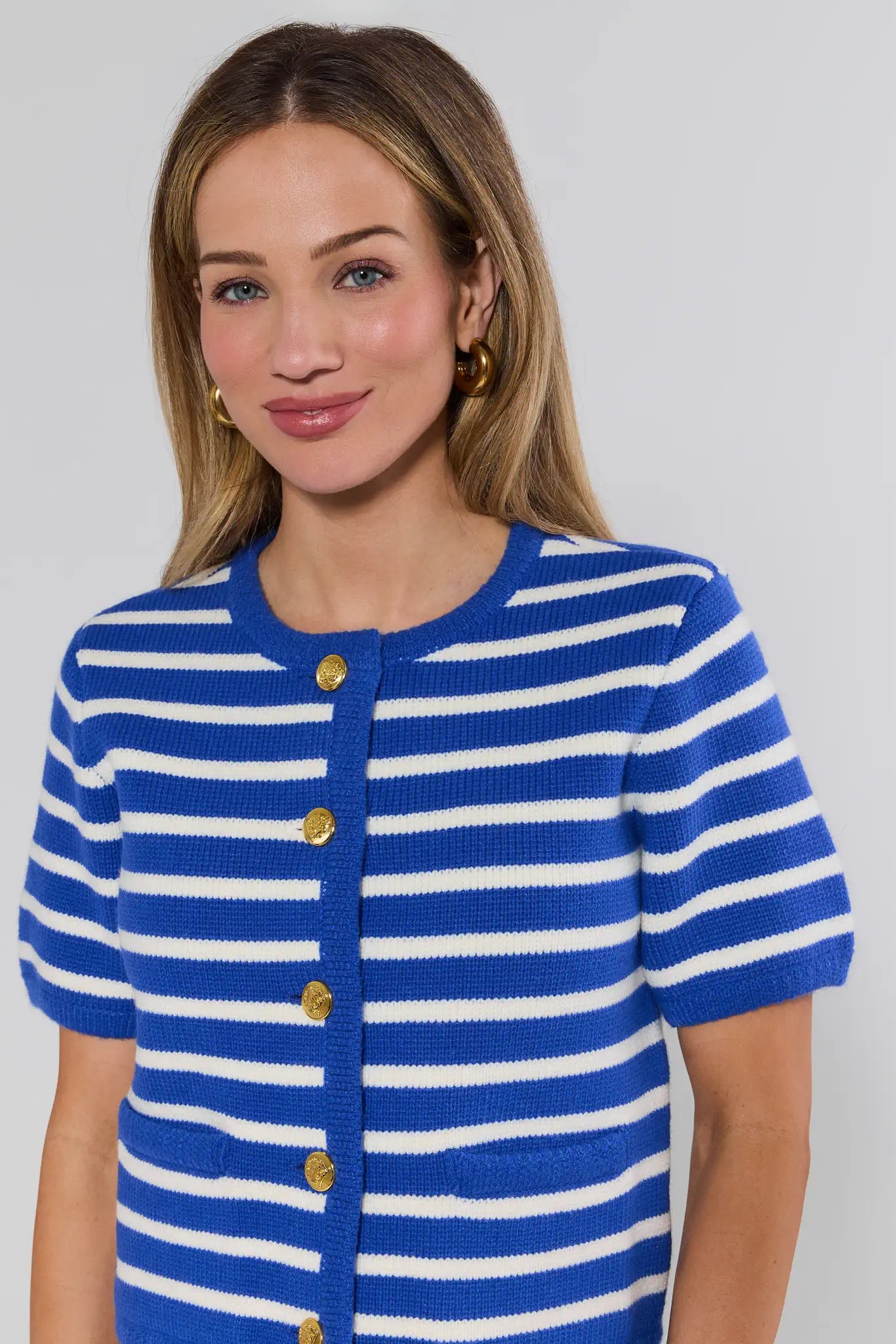 Woman wearing a blue and white striped cardigan with gold buttons on a plain background