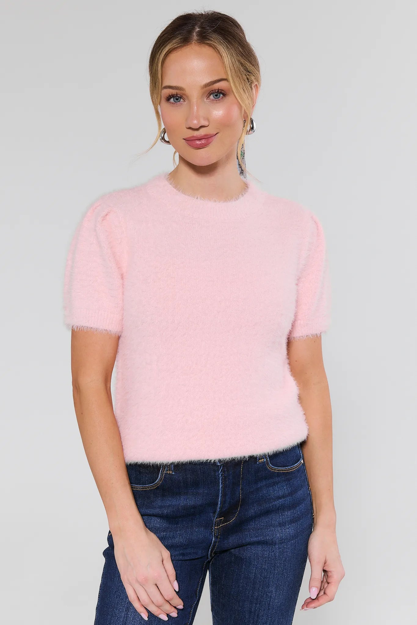 Woman wearing a pink sweater and blue jeans on a plain background