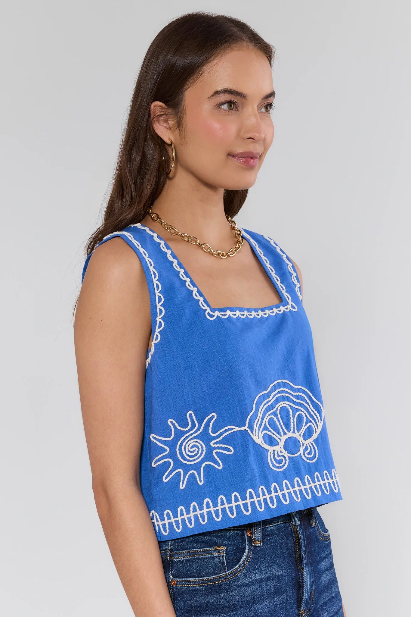 Woman wearing a blue sleeveless top with white patterns on a plain background