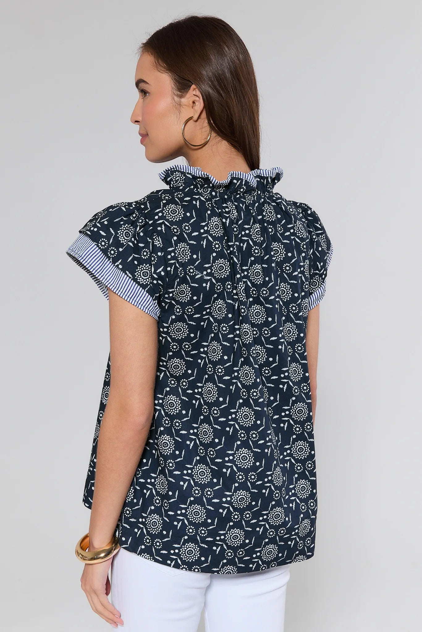 Woman wearing a navy patterned blouse with white pants on a plain background