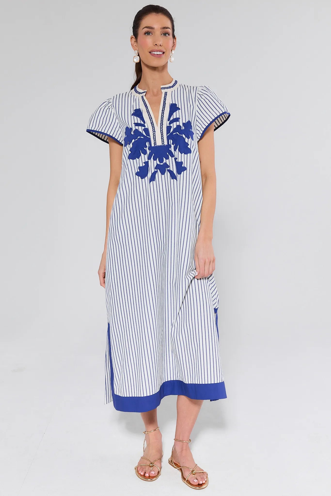 Woman wearing a white dress with blue stripes and floral patterns on a plain background