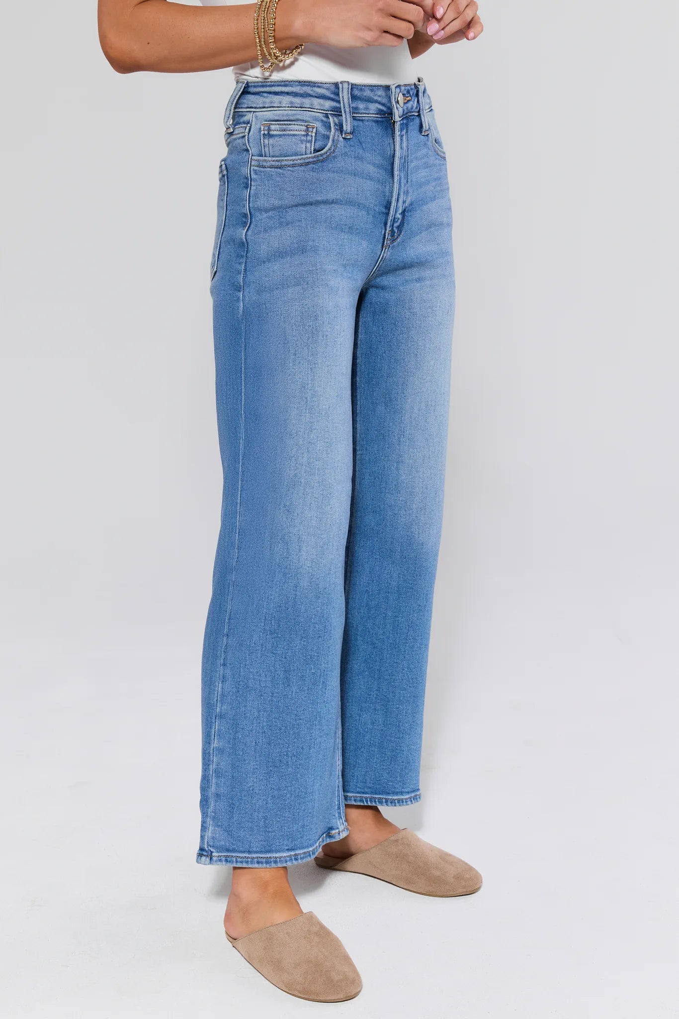 Person wearing blue jeans and beige shoes on a white background