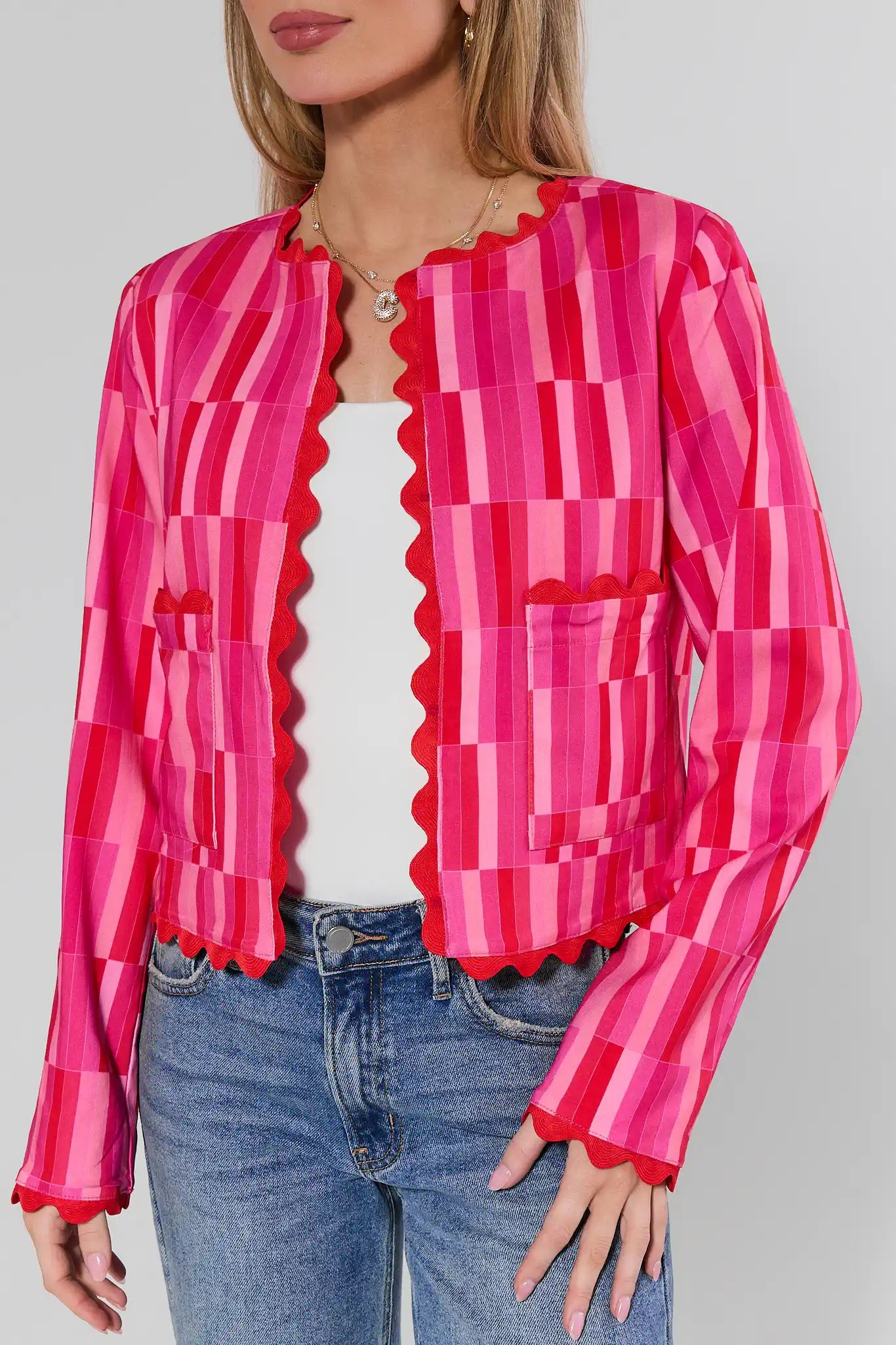 Woman wearing a bright pink and red patterned blouse with blue jeans on a plain background