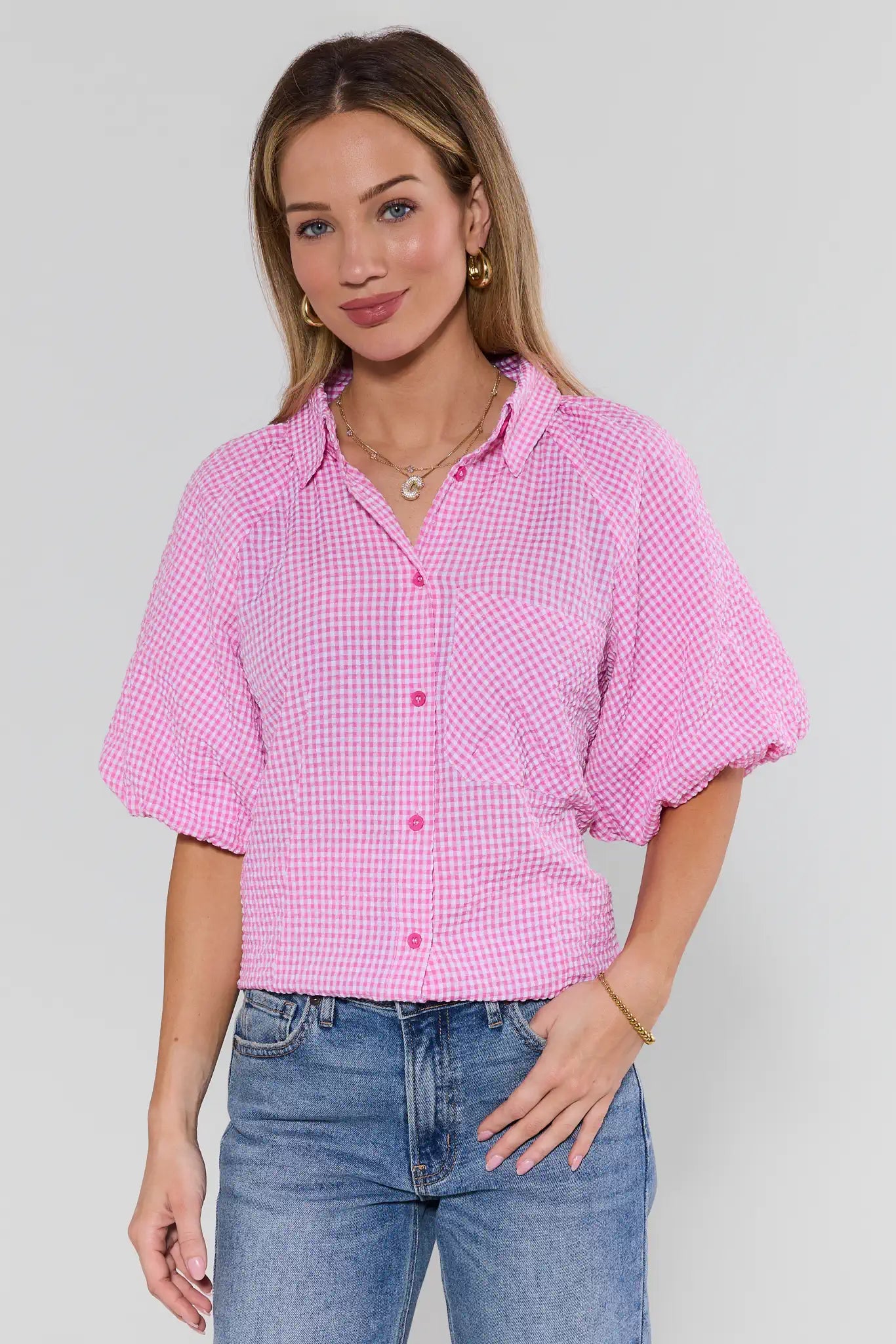 Woman wearing a pink checkered shirt and blue jeans against a plain background