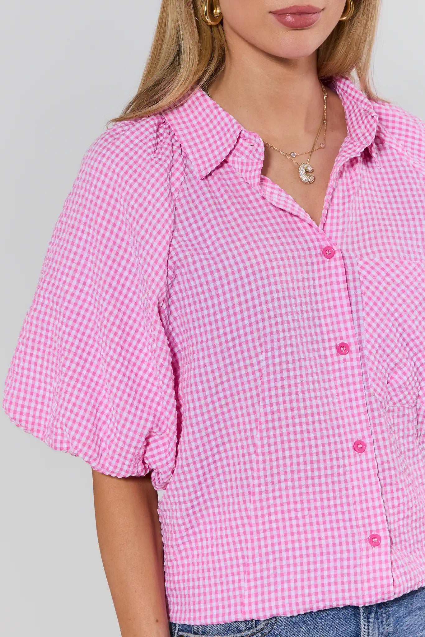 Woman wearing a pink checkered shirt with short sleeves on a gray background