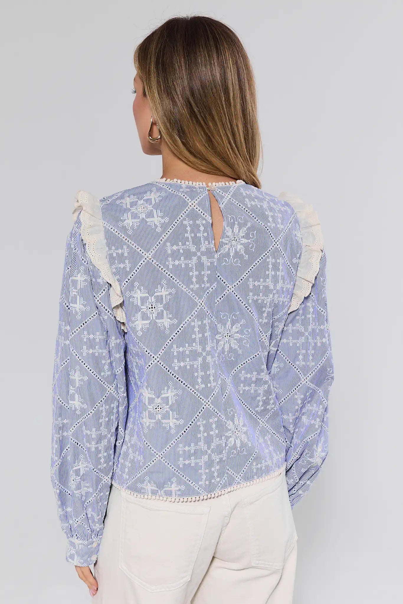 Woman wearing a blue embroidered top with white pants on a gray background