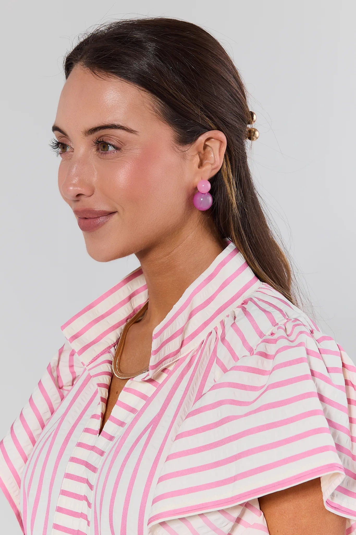 Woman wearing pink and white striped shirt with pink earrings against a plain background