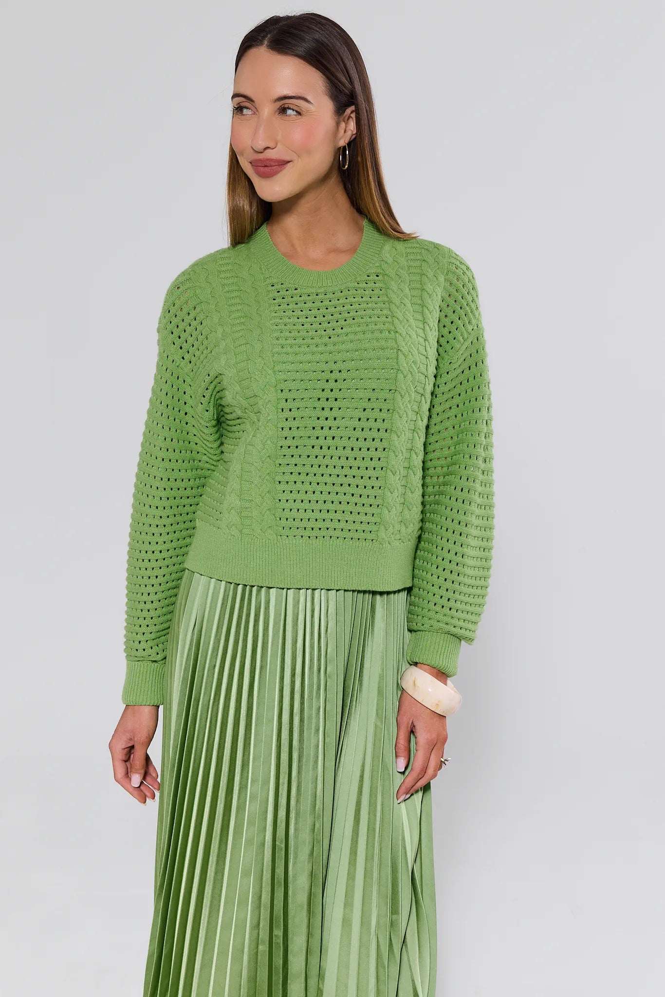 Woman wearing a green knitted sweater and pleated skirt against a white background