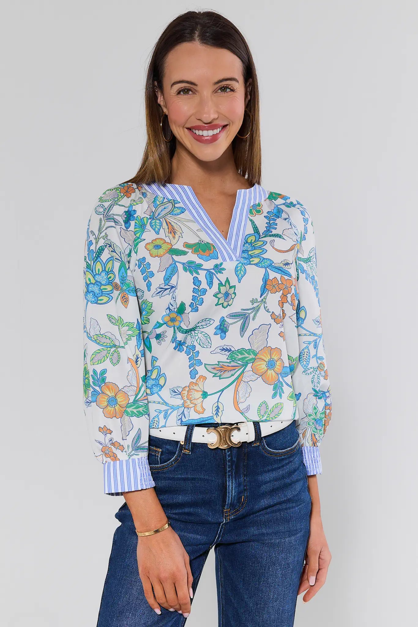 Woman wearing a floral blouse and blue jeans against a white background