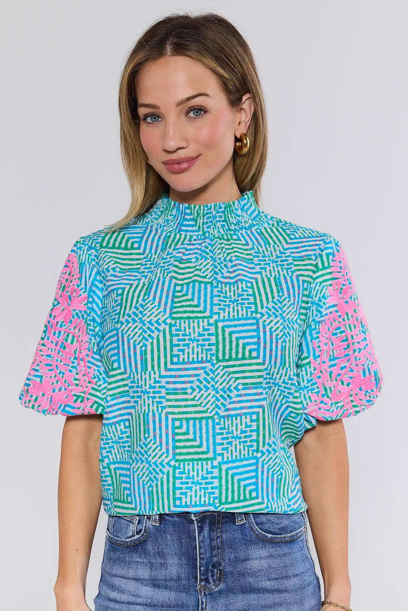 Woman wearing a colorful geometric patterned top against a plain background