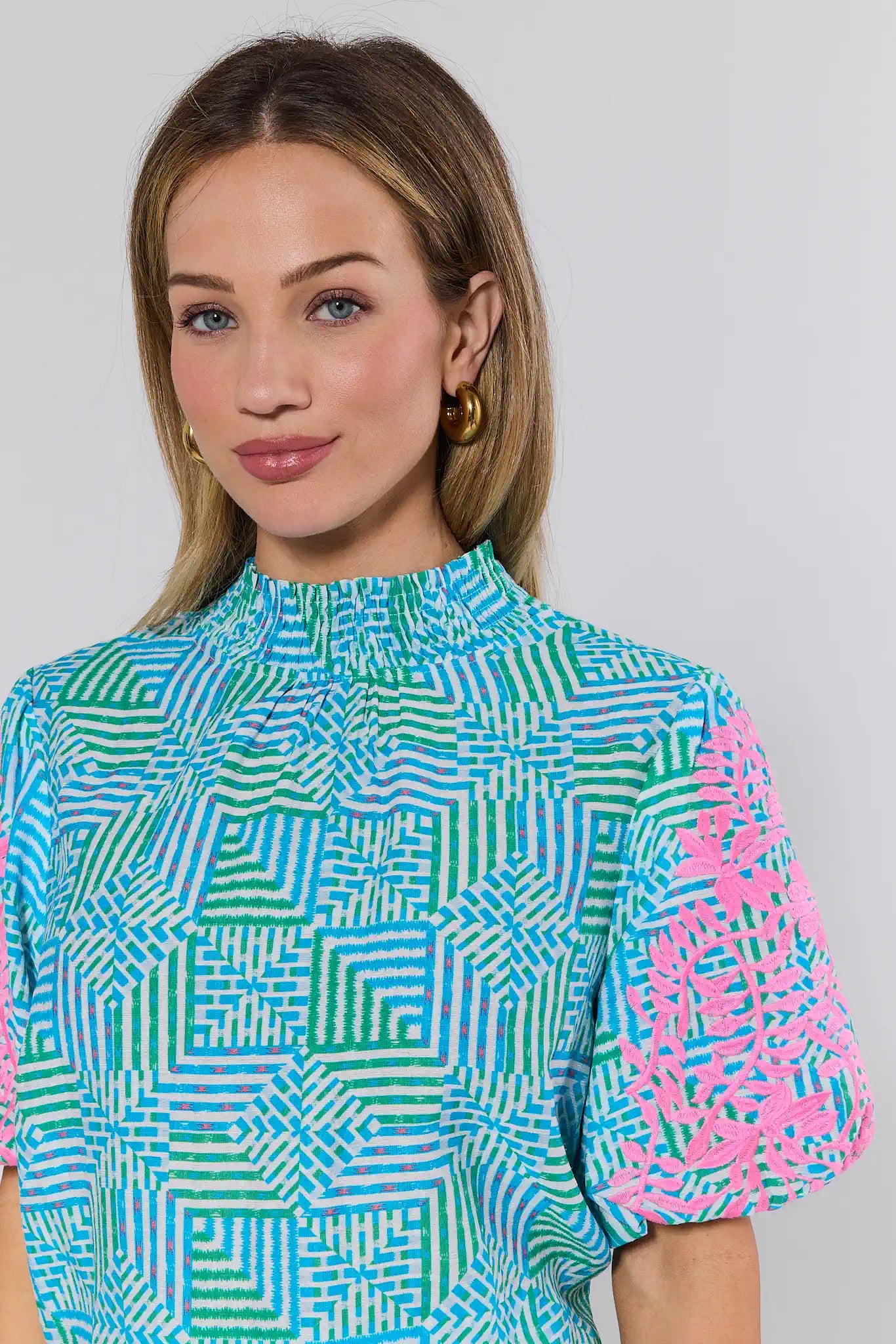 Woman wearing a colorful geometric patterned top against a plain background