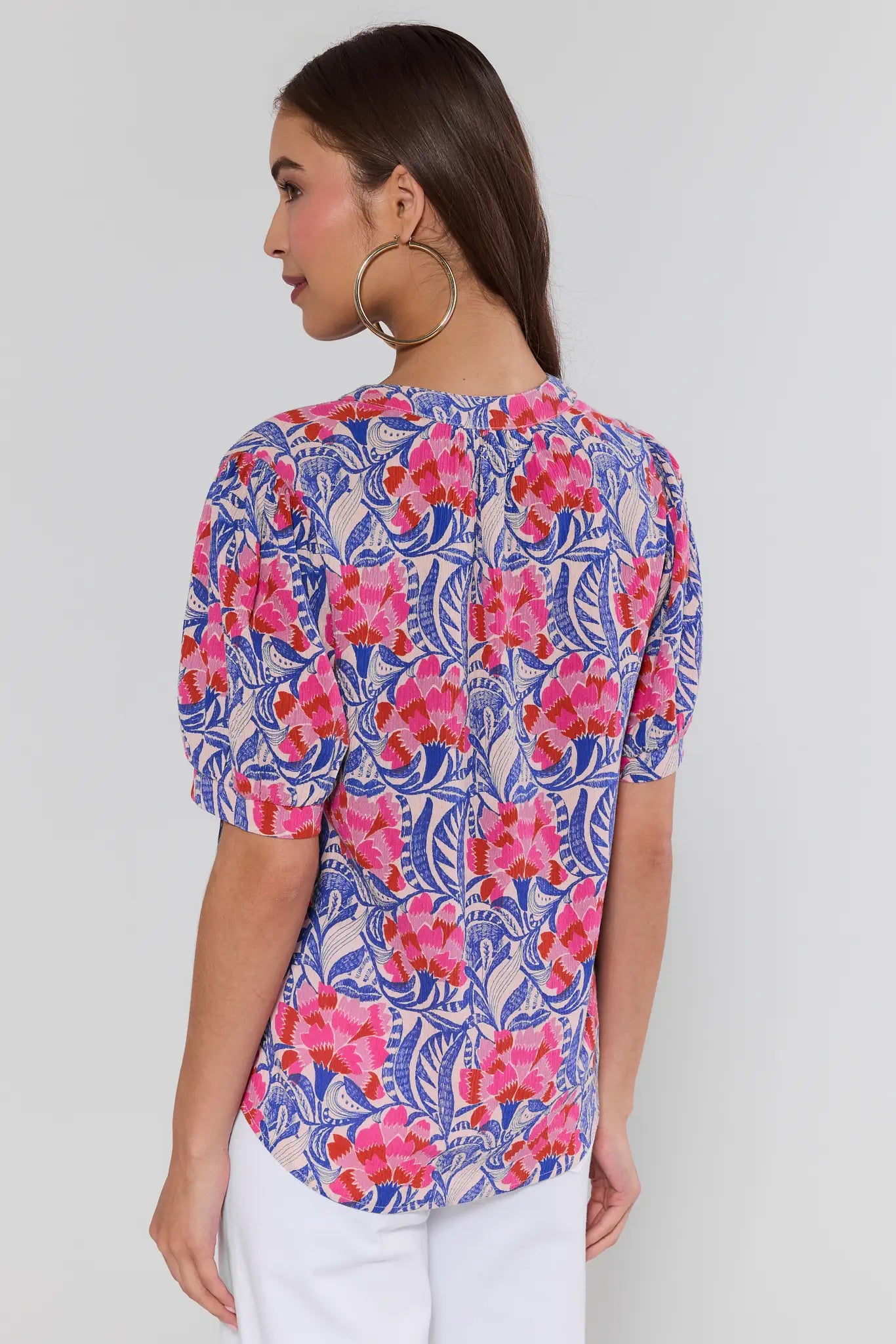 Woman wearing a floral patterned top with pink and blue flowers on a plain background