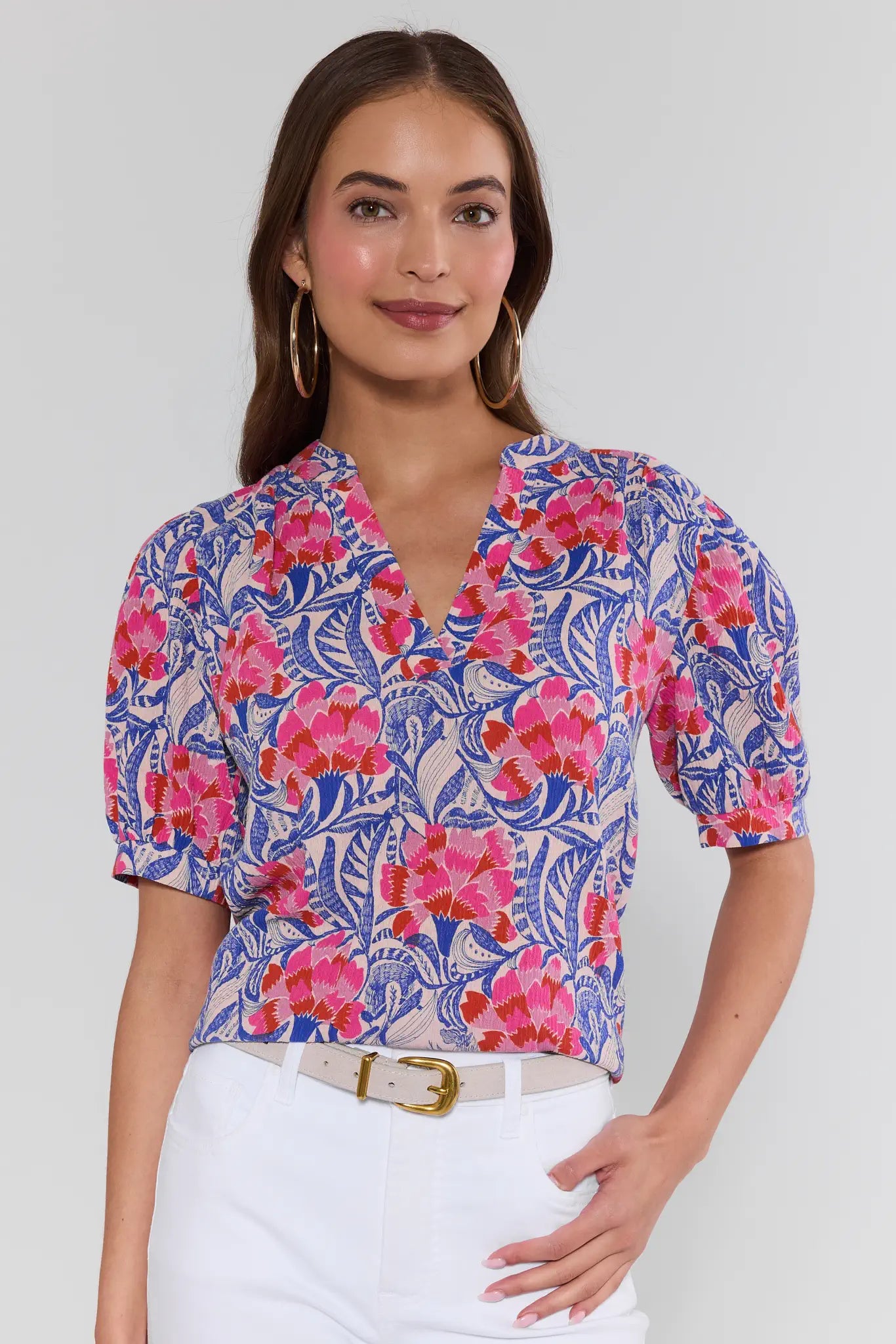 Woman wearing a colorful floral blouse with white pants on a plain background