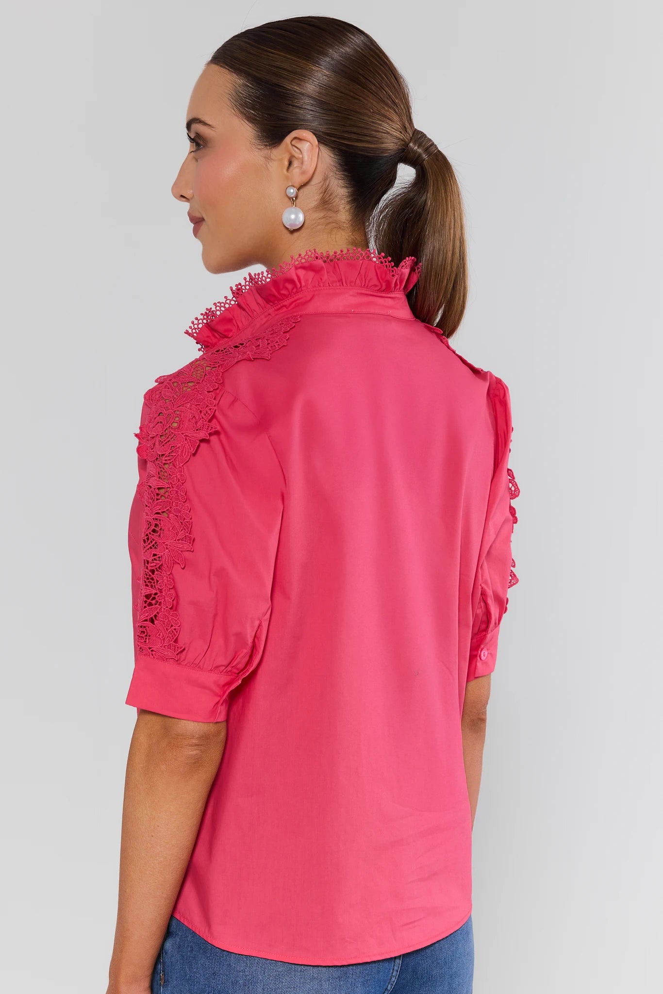 Woman wearing a pink blouse with ruffled details on a plain background