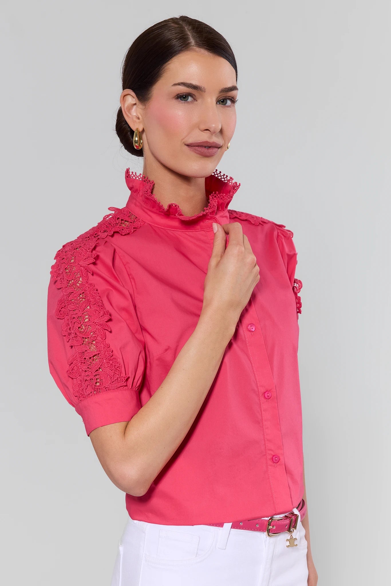 Woman wearing a pink blouse with lace details on a gray background