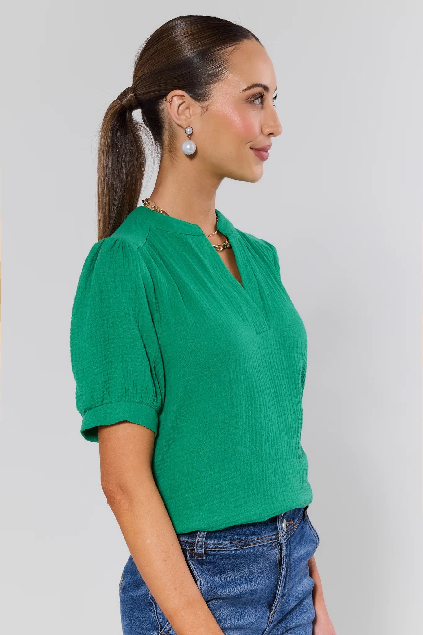 Woman wearing a green blouse and blue jeans against a plain background