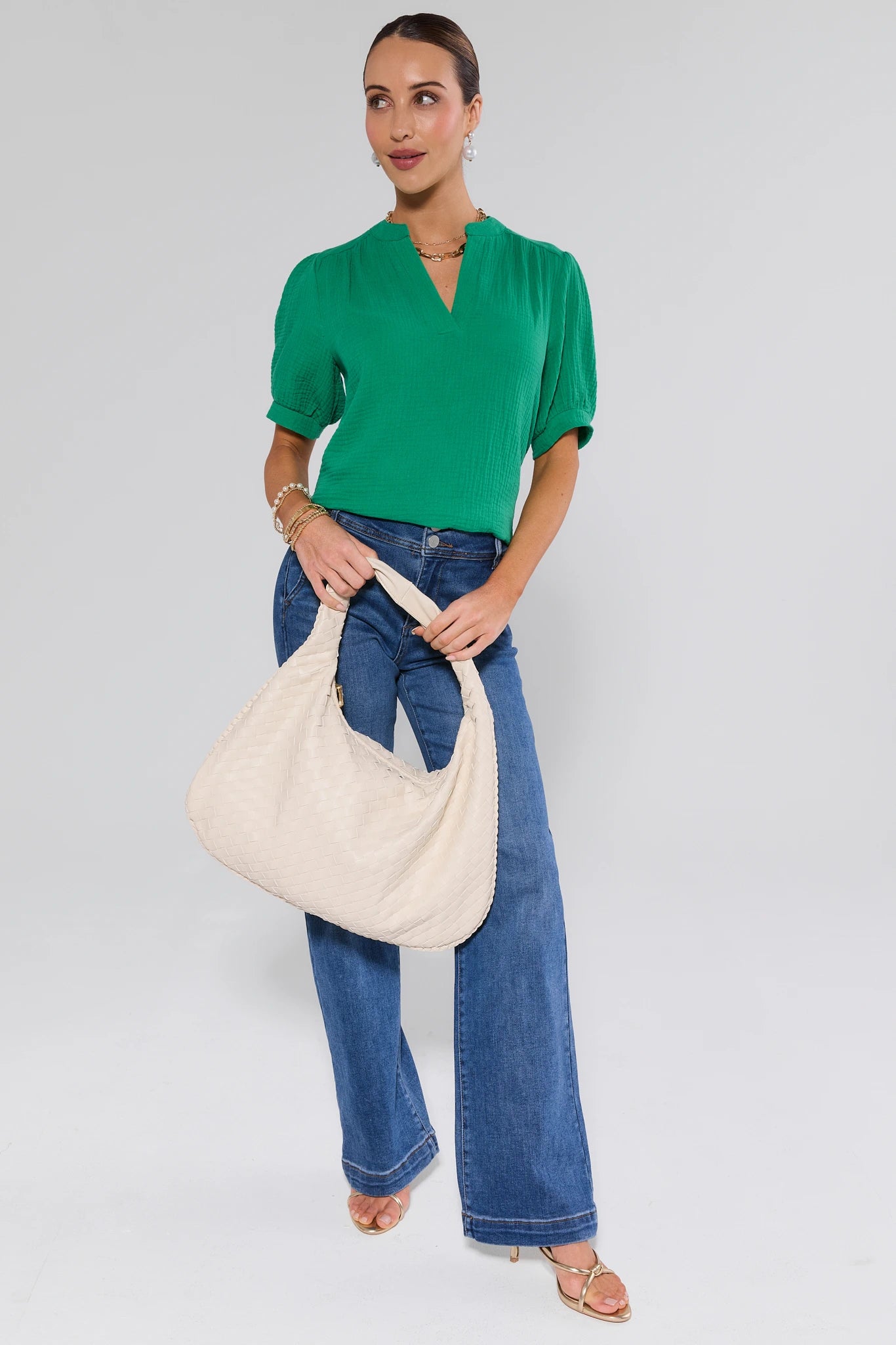 Woman holding a beige tote bag wearing a green top and blue jeans on a white background