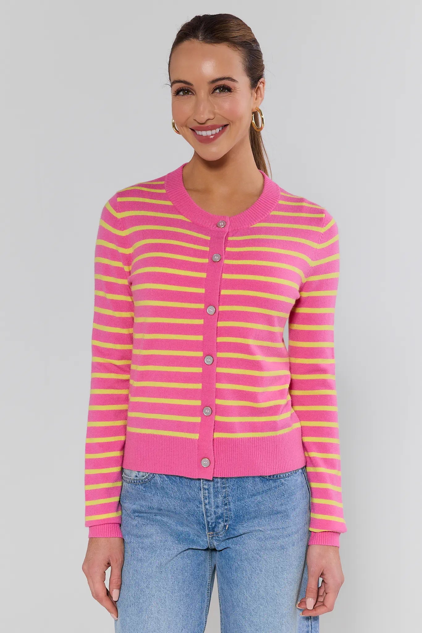 Woman wearing a pink and yellow striped cardigan with blue jeans on a plain background