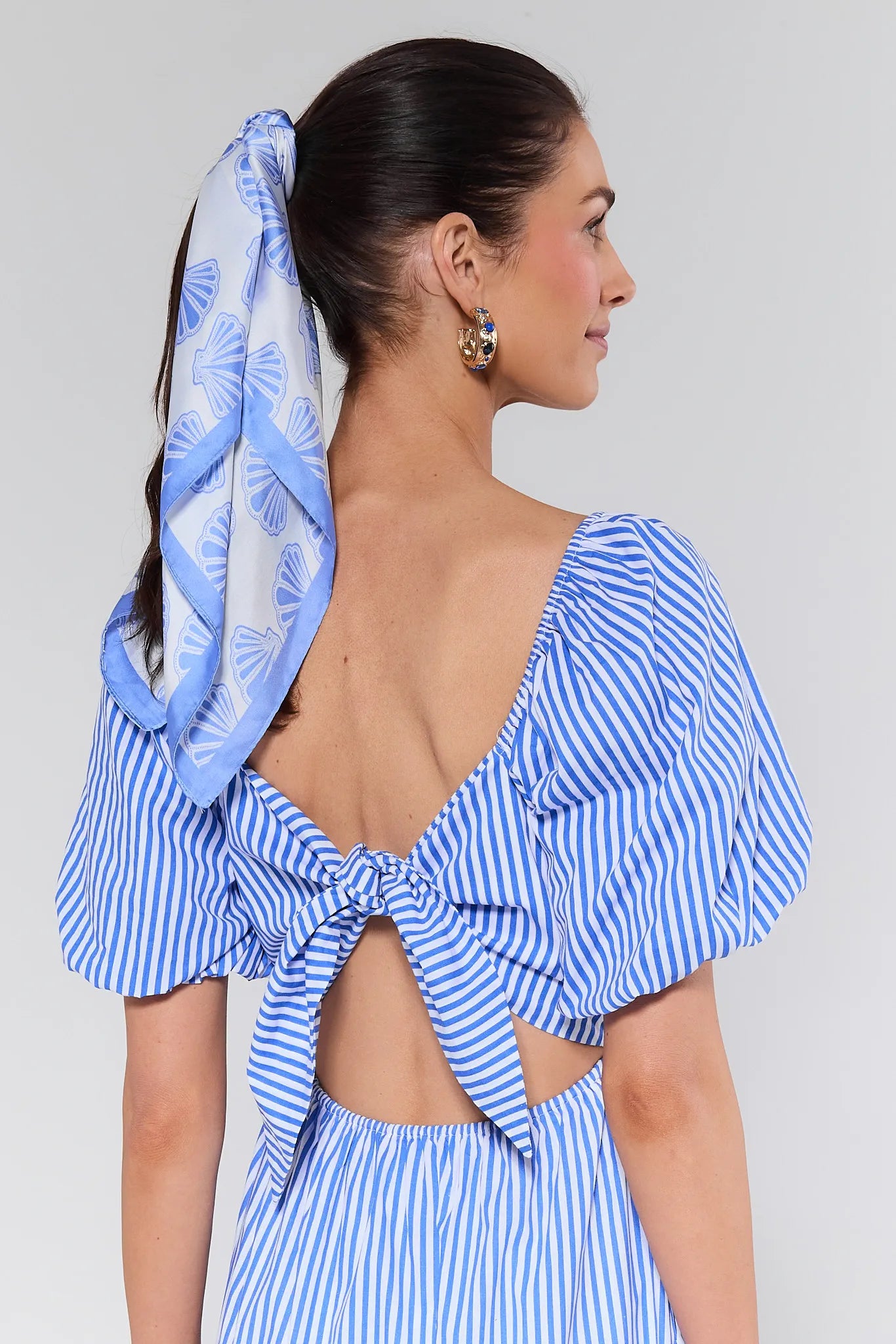 Woman wearing a blue and white striped dress with a headscarf on a plain background