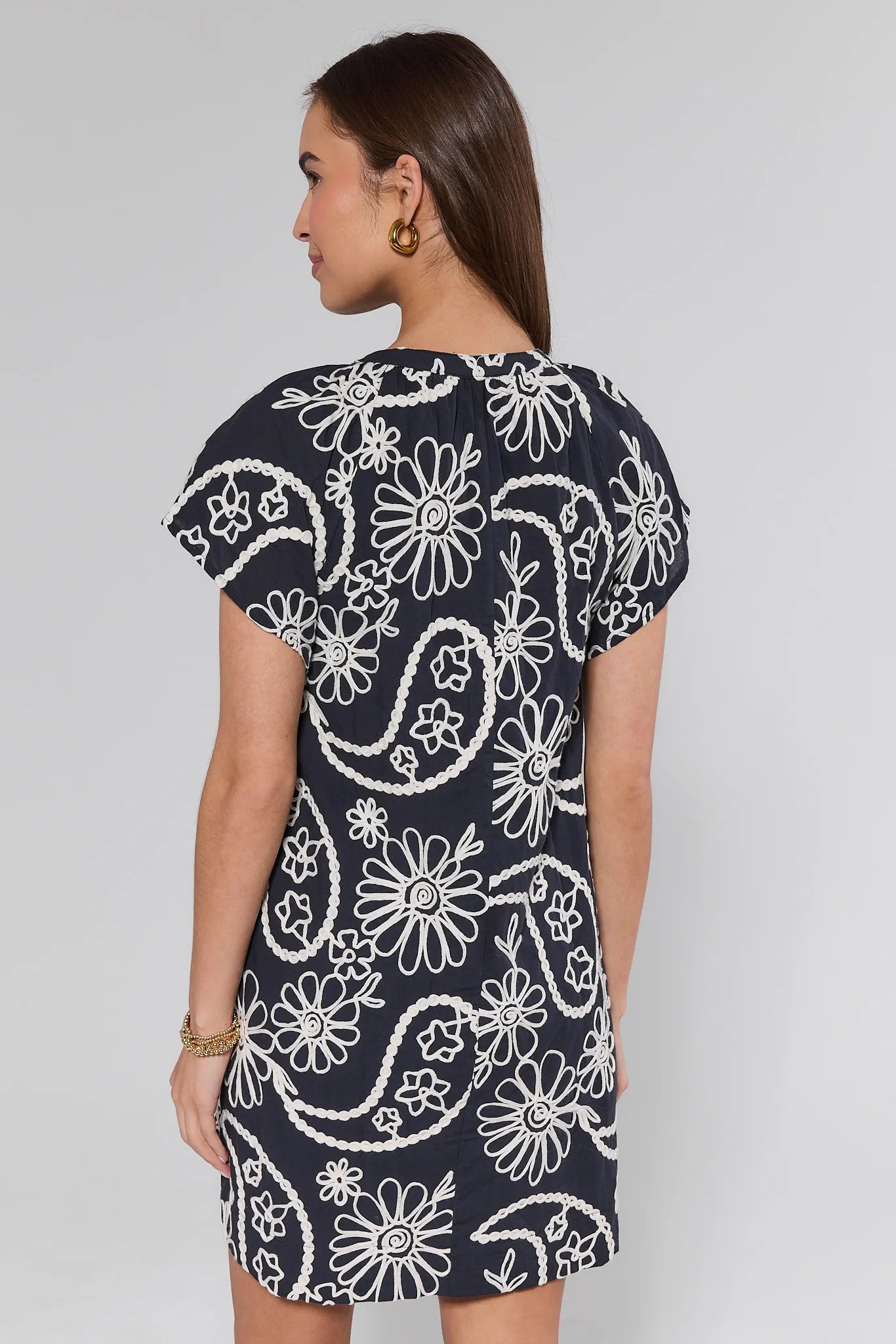 Woman wearing a navy dress with white floral patterns on a plain background