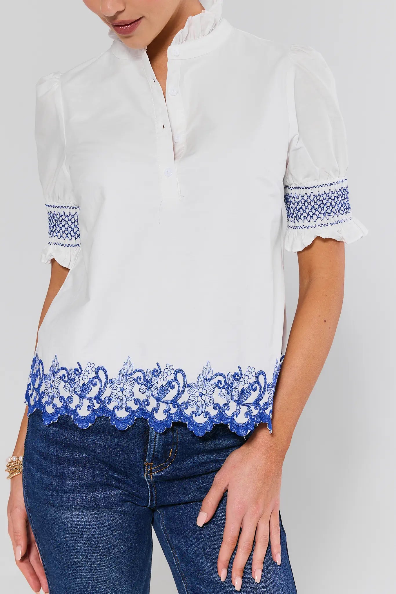 White blouse with blue embroidery details worn by a person on a white background