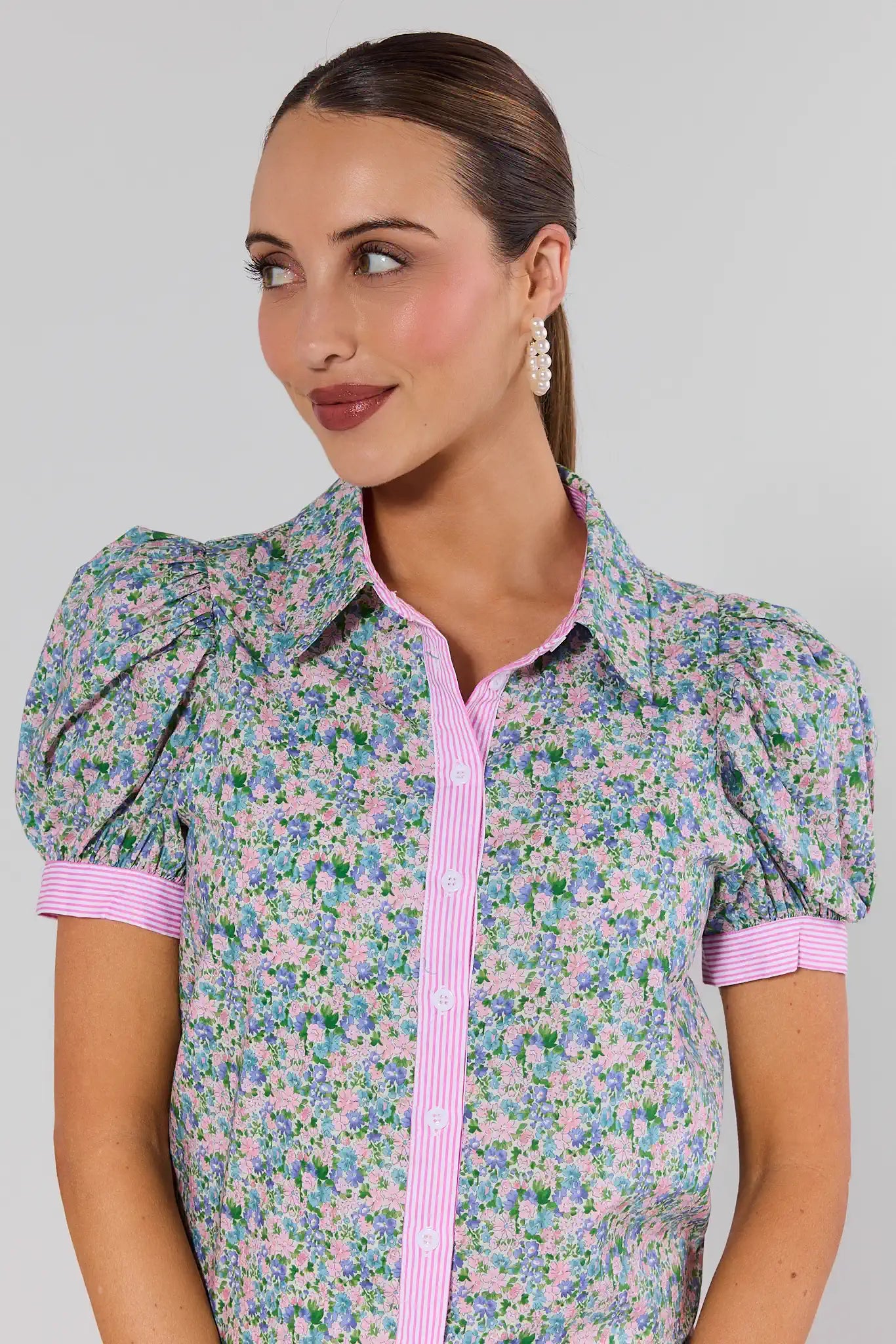 Woman wearing a floral blouse with pink trim on a gray background