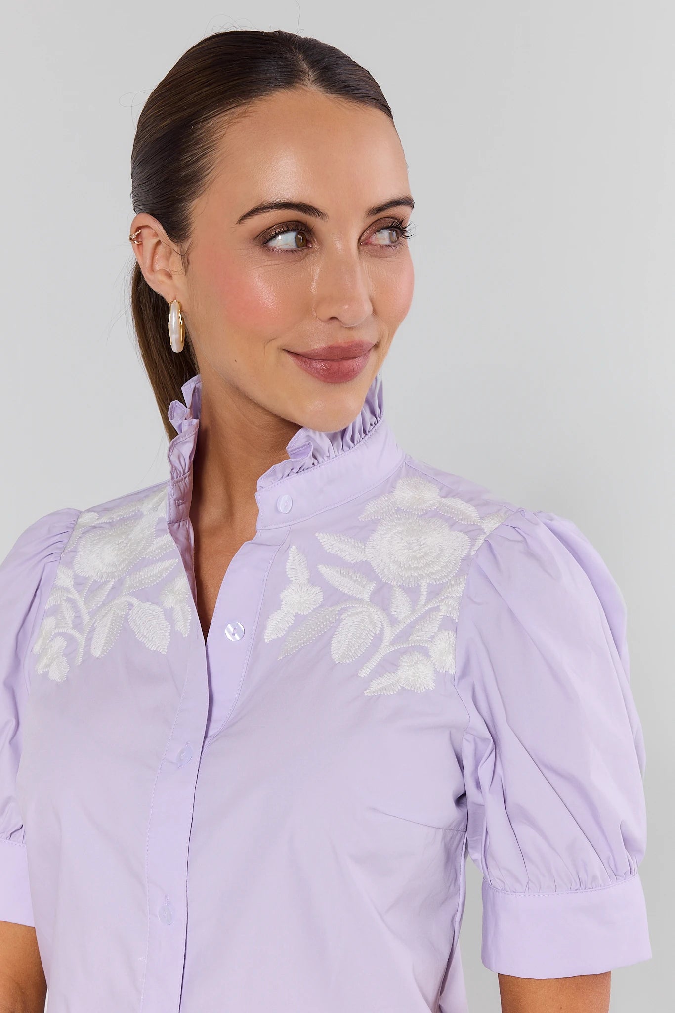 Woman wearing a light purple blouse with floral embroidery on a plain background