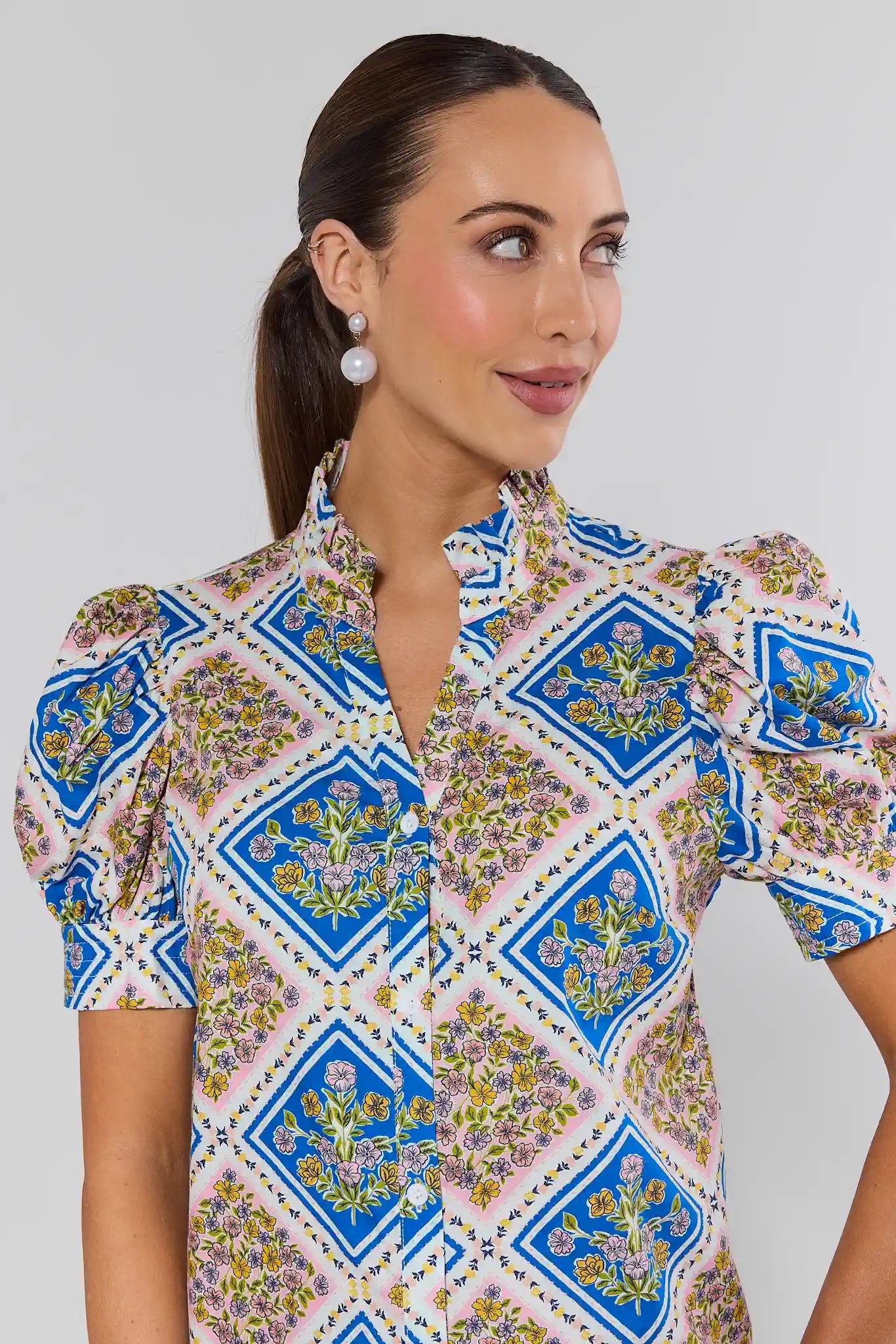 Woman wearing a patterned shirt with blue geometric and floral design on a plain background