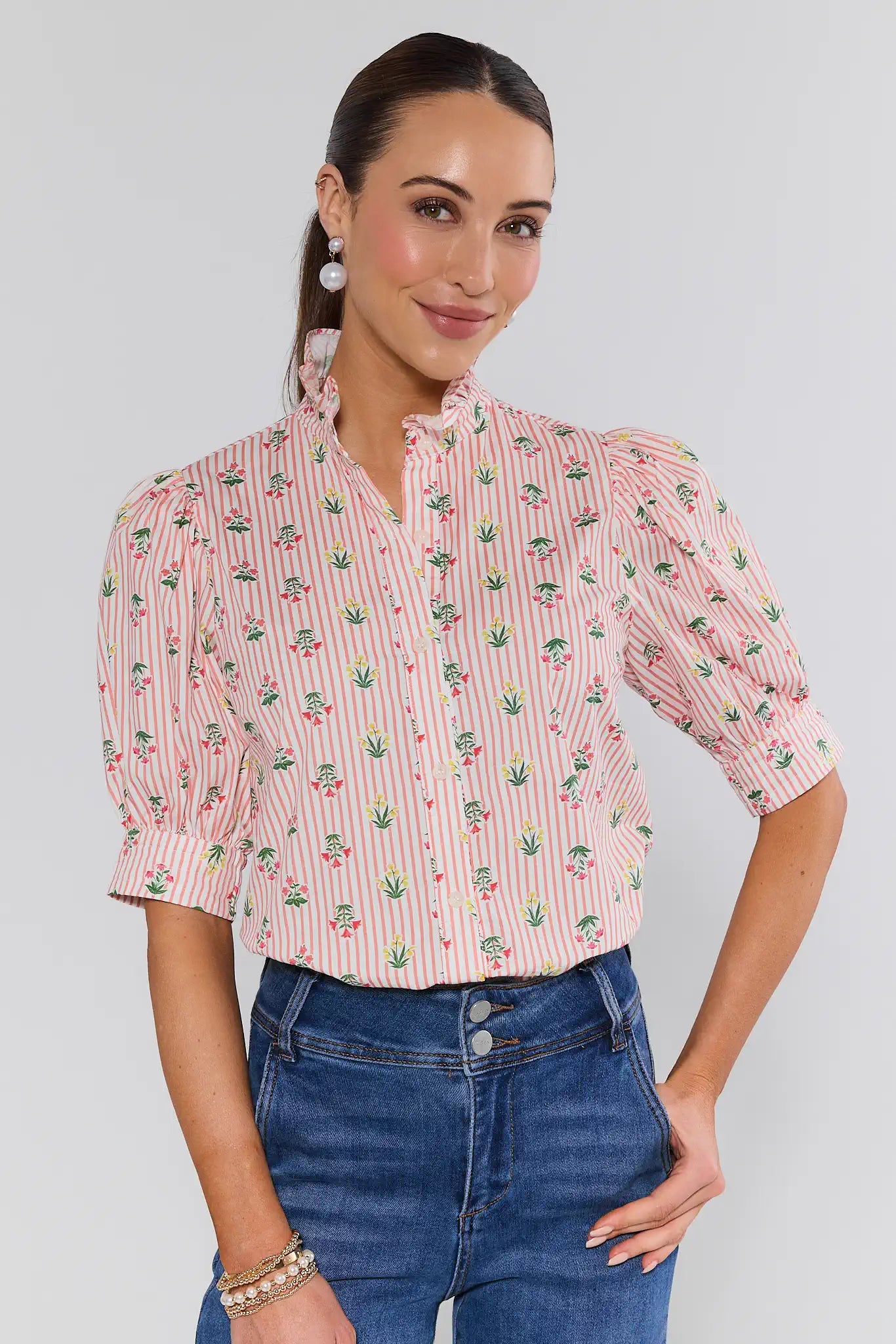 Woman wearing a pink patterned blouse and blue jeans against a plain background