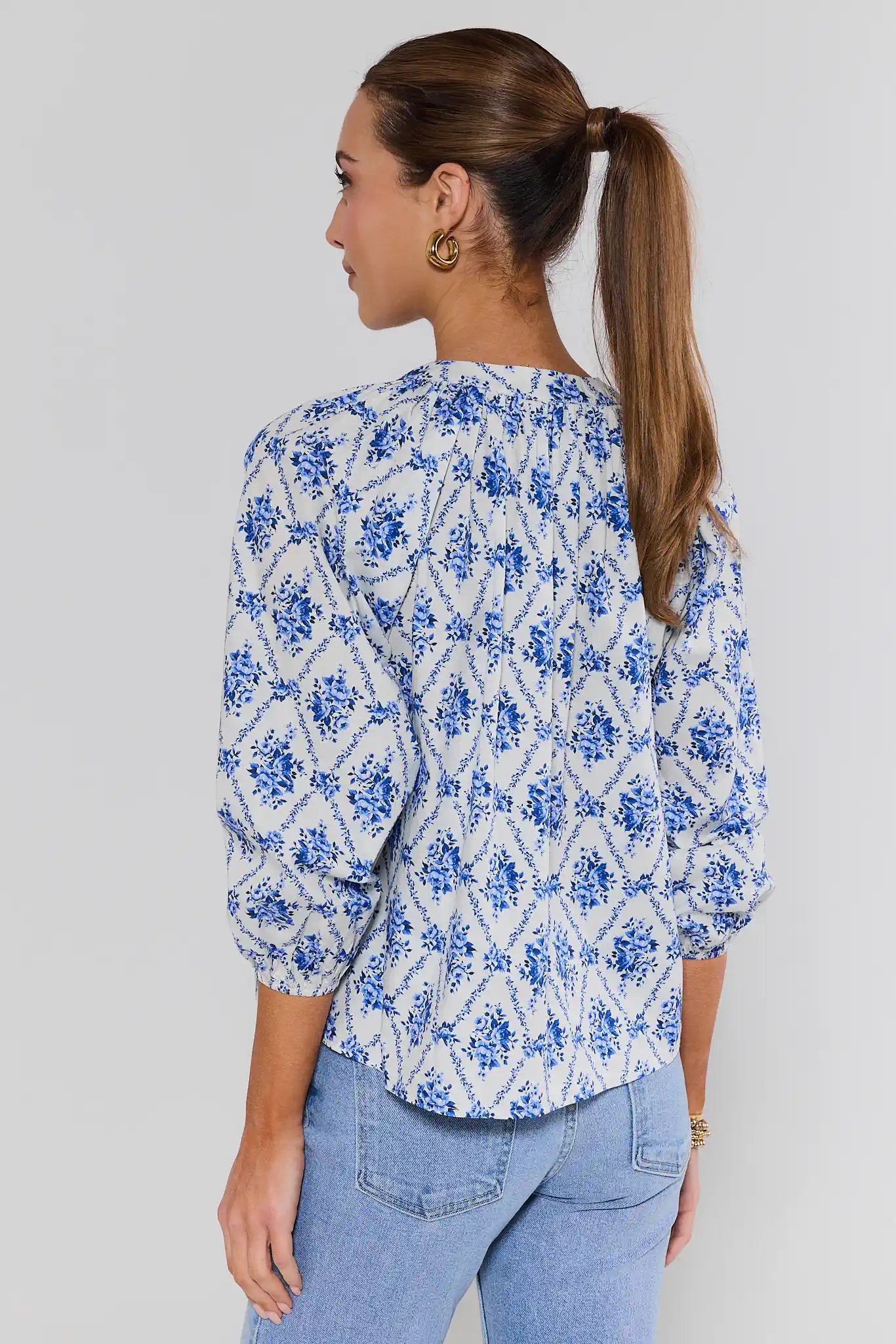 Woman wearing a blue floral blouse and light blue jeans against a gray background