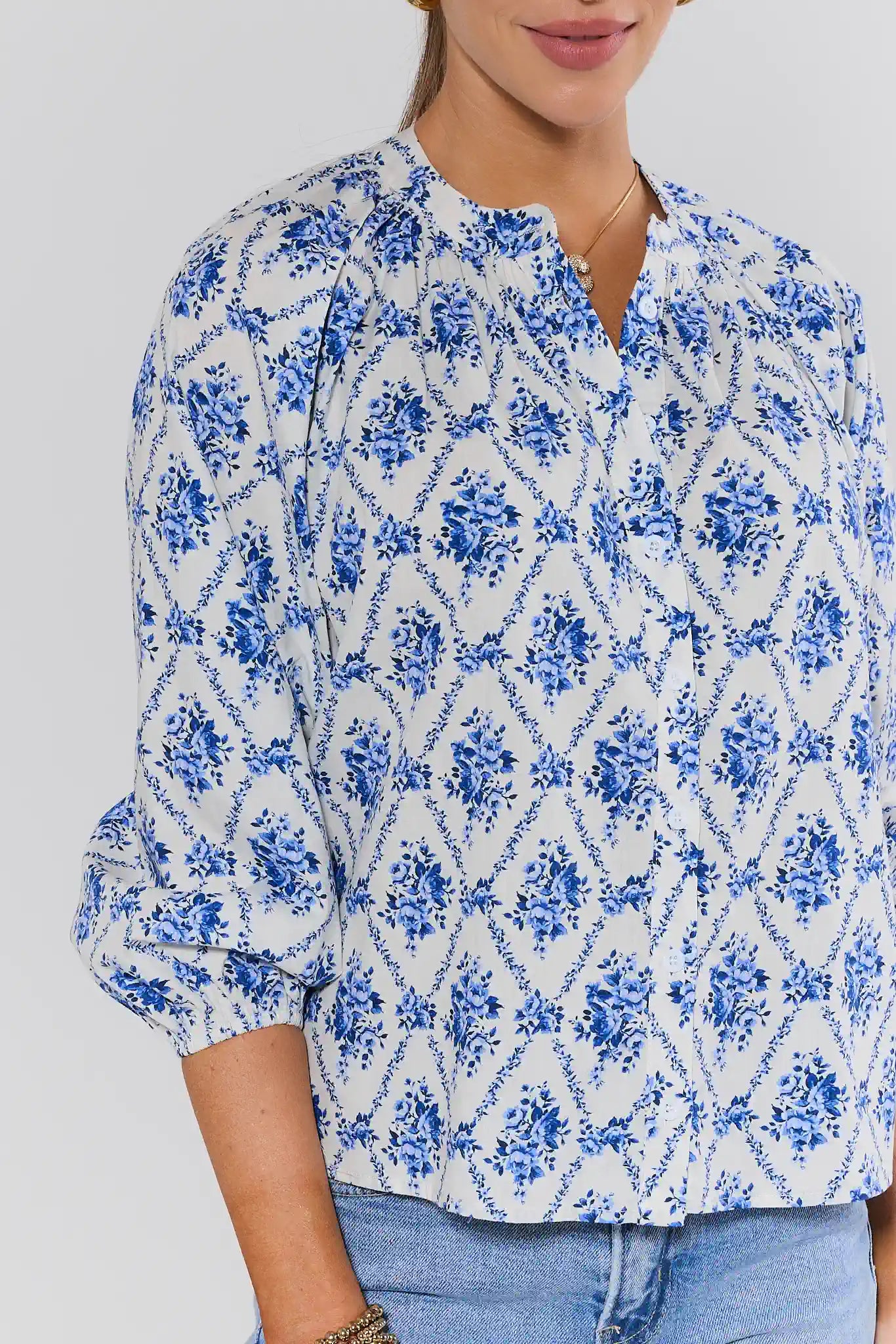 Woman wearing a blue and white floral patterned blouse against a plain background