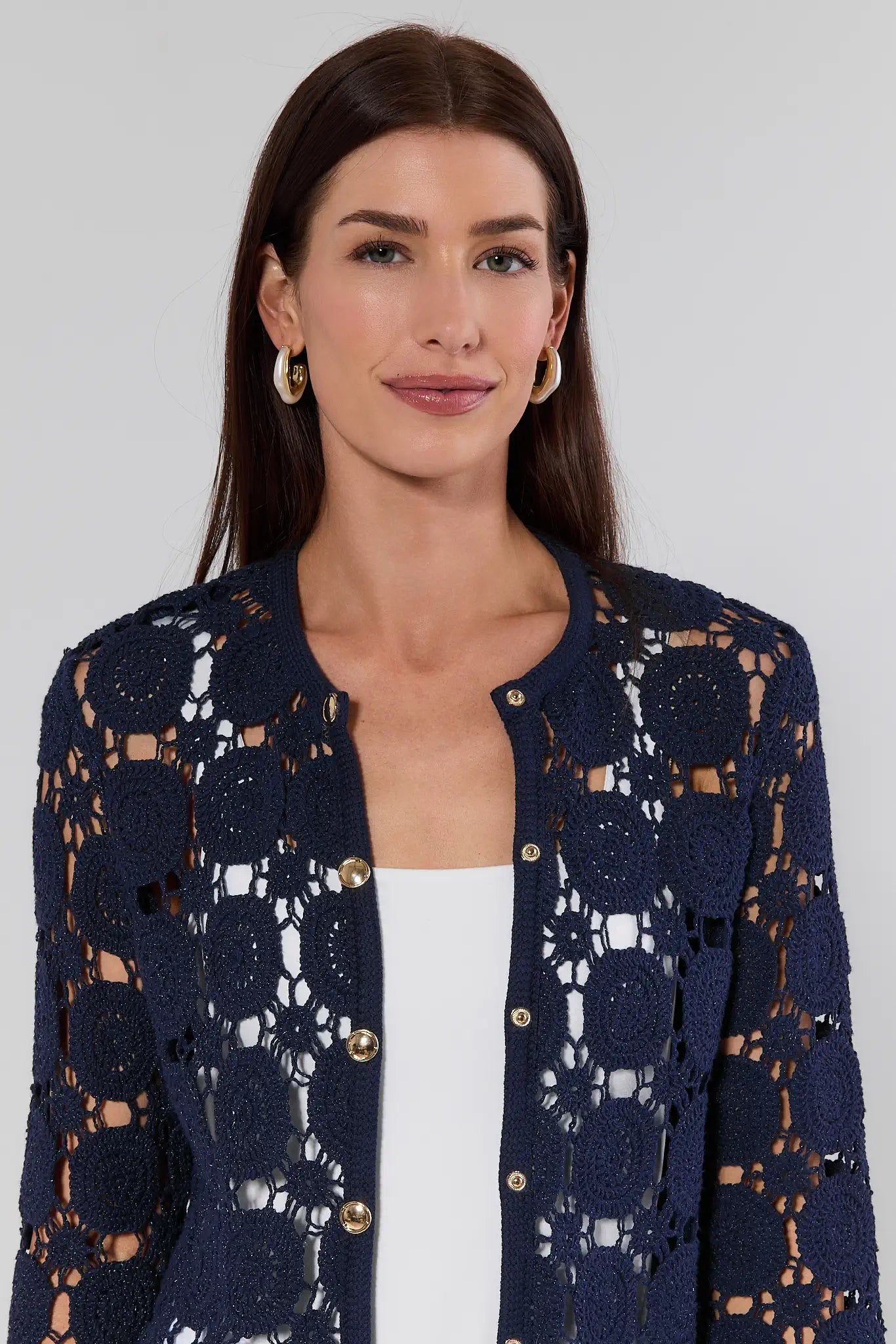Woman wearing a navy blue lace cardigan over a white top against a plain background