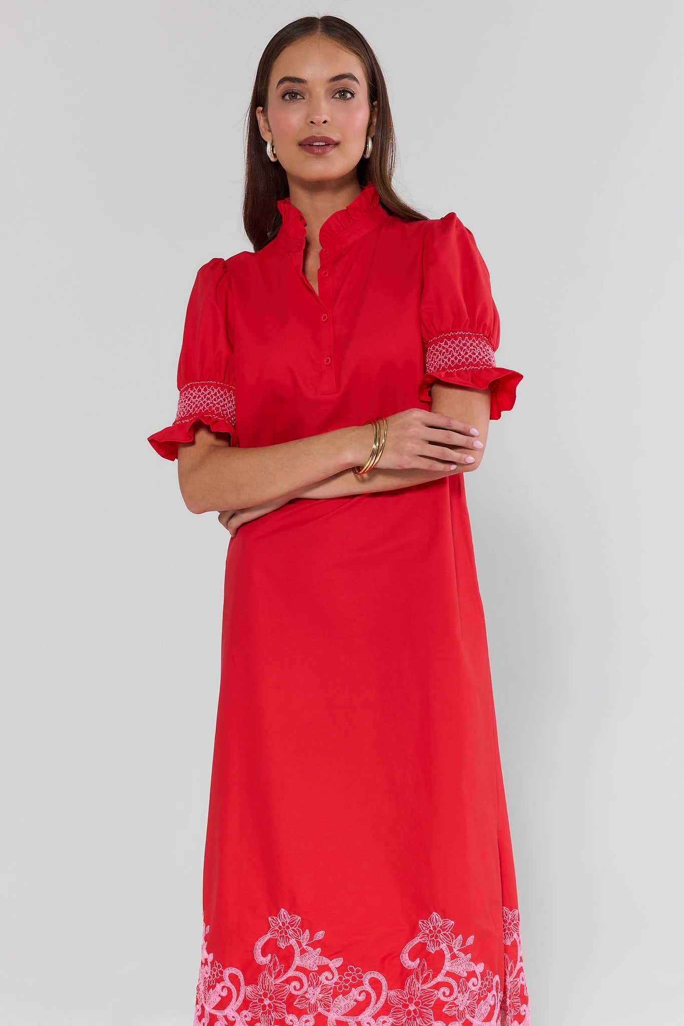 Woman wearing a red dress with white embroidery on a plain background