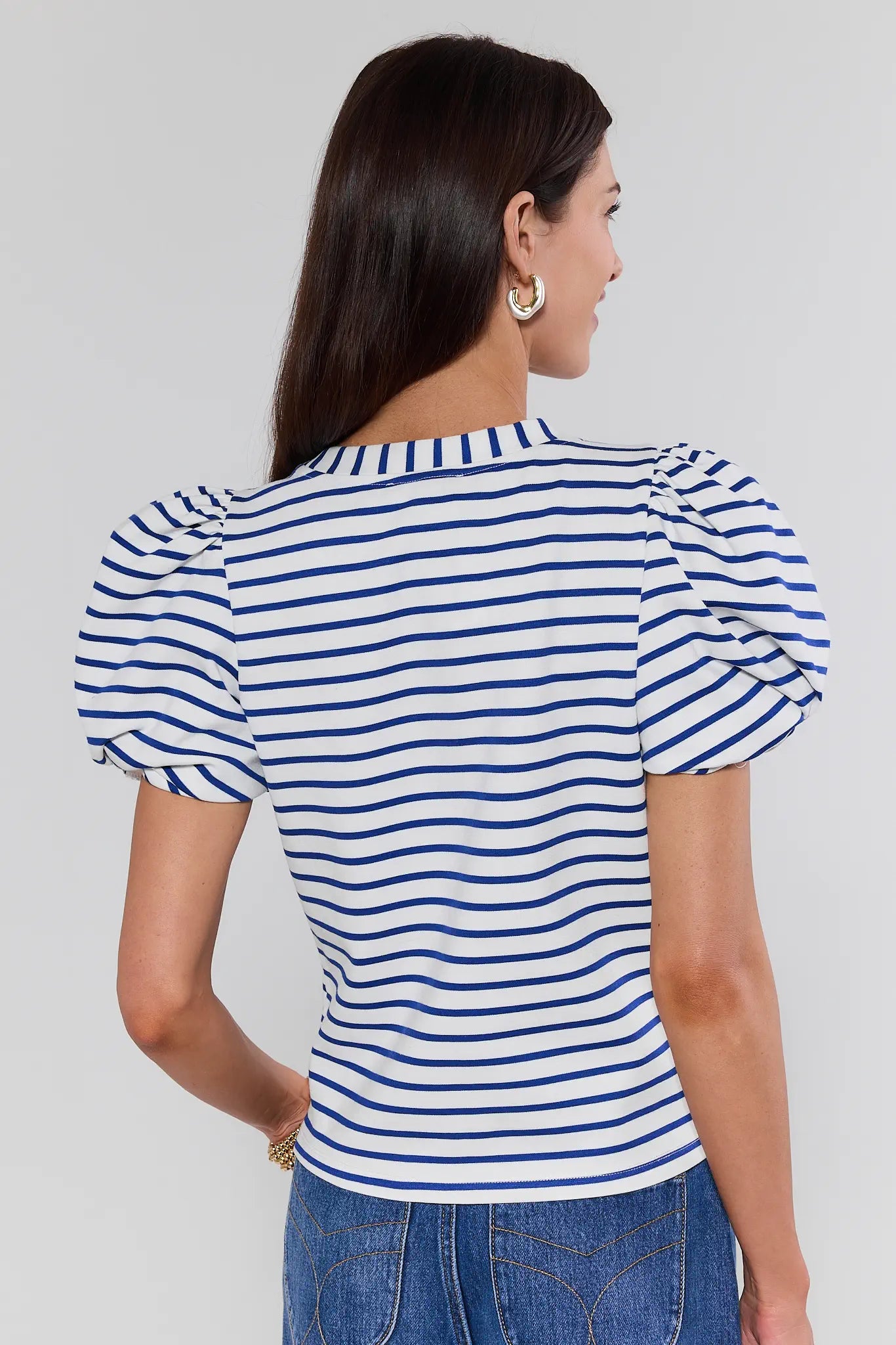 Woman wearing a blue and white striped top with puffed sleeves on a gray background
