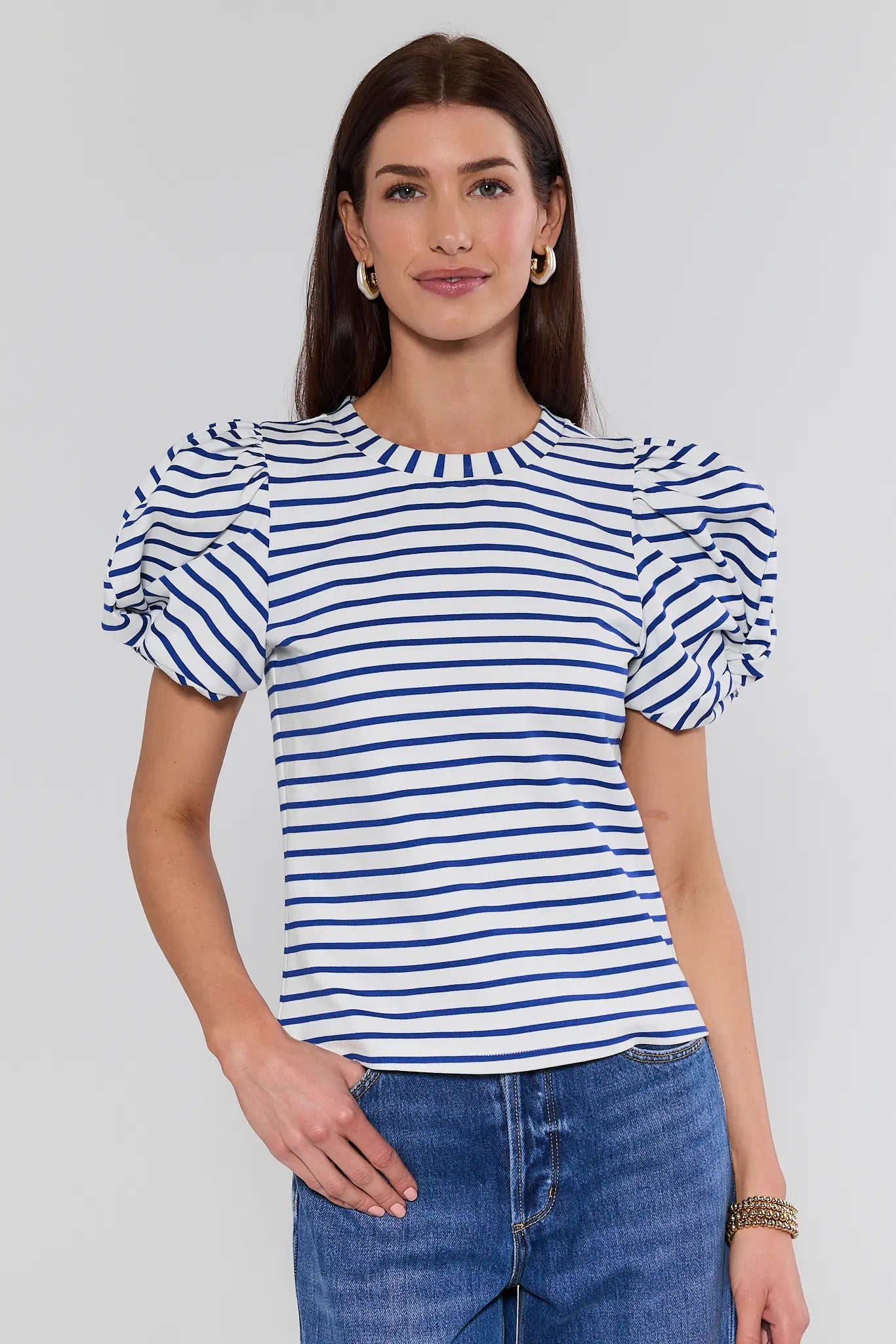 Woman wearing a blue and white striped shirt with puffed sleeves on a plain background