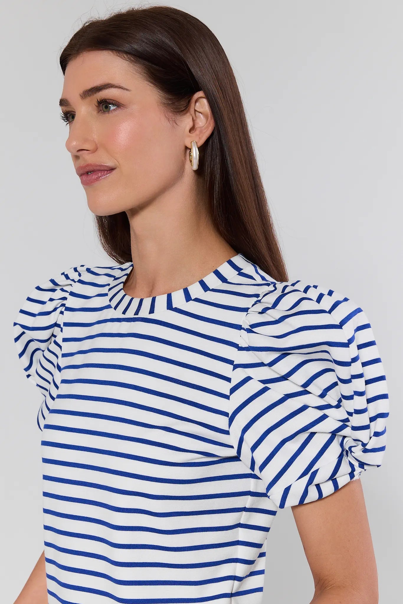 Woman wearing a blue and white striped top with puffed sleeves on a plain background